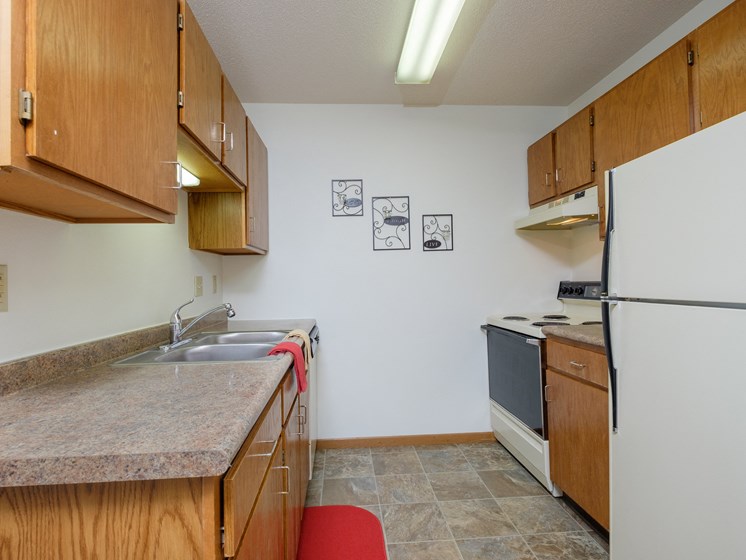 a kitchen with wooden cabinets and a sink and a refrigerator. Fargo, ND Oak Court Apartments