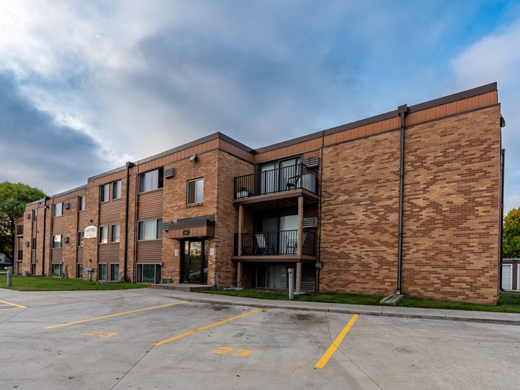 a brick apartment building with a parking lot and a cloudy sky. Fargo, ND Hartford Apartments