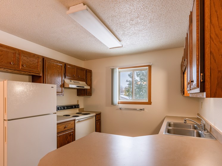 A kitchen with white appliances and wooden cabinets. Fargo, ND Huntington Apartments.