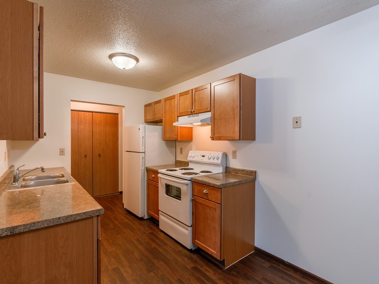 A kitchen with wooden cabinets and white appliances and a sink. Fargo, ND Long Island Apartments.