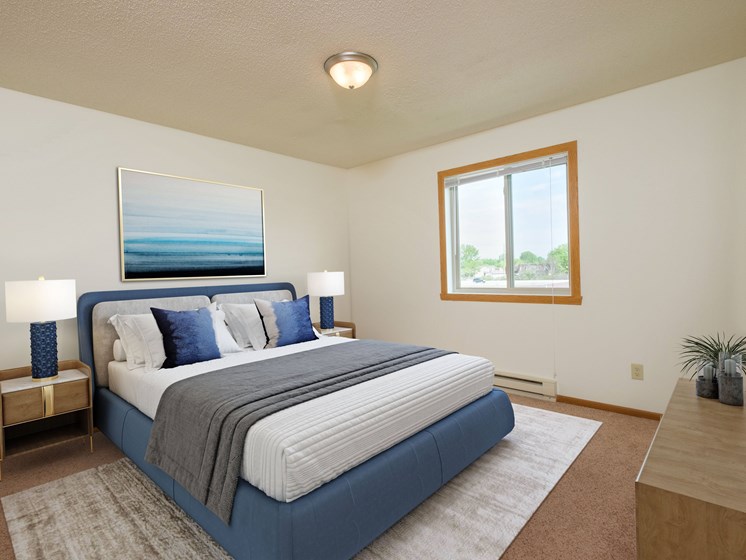 a bedroom with a blue and white bed and a window. Fargo, ND Oak Court Apartments