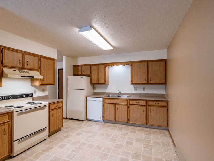 an empty kitchen with white appliances and wooden cabinets. Fargo, ND West Oak Apartments.