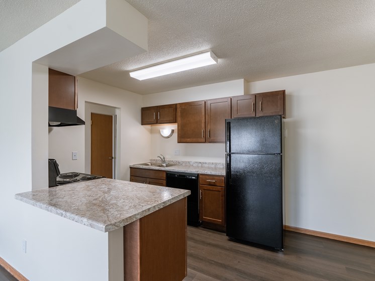 an empty kitchen with a counter top and a black refrigerator. Fargo, ND North Manor Apartments