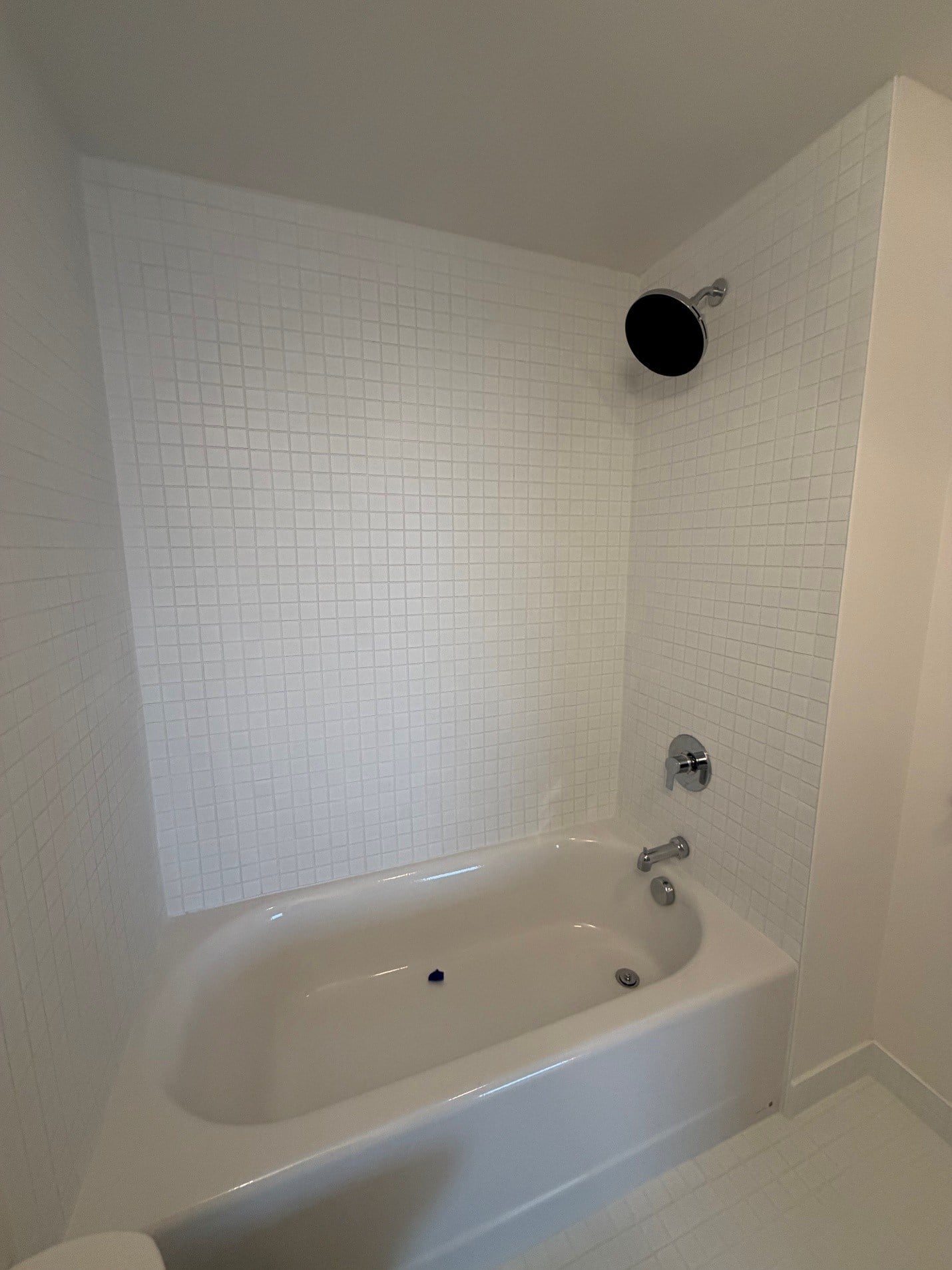 A white bathroom with a white tub and a white tiled wall.