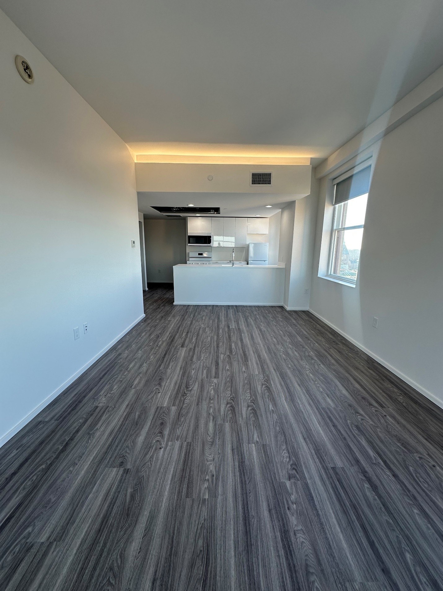 A room with a wooden floor and a kitchen in the background.