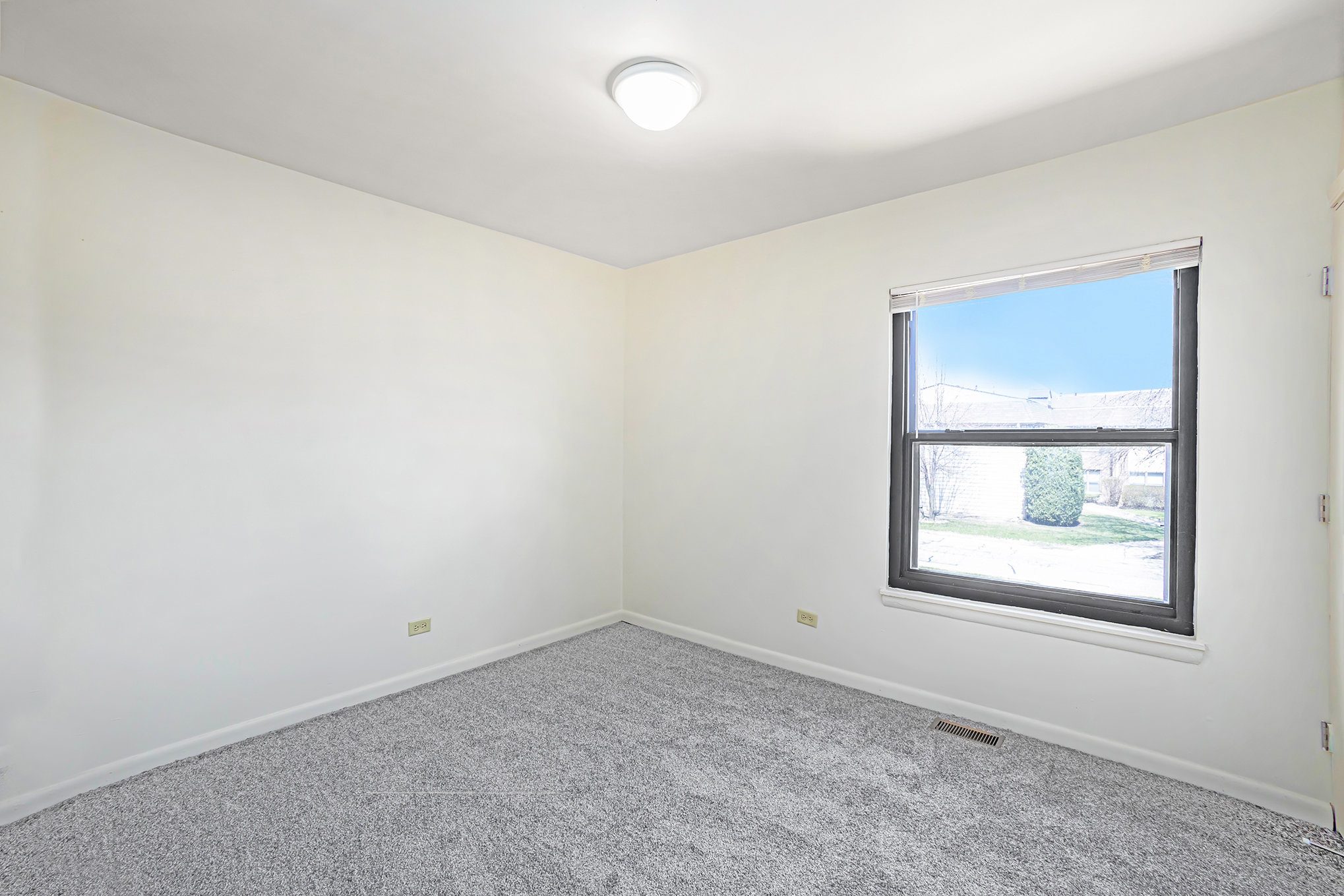 A room with a window and a grey carpet.