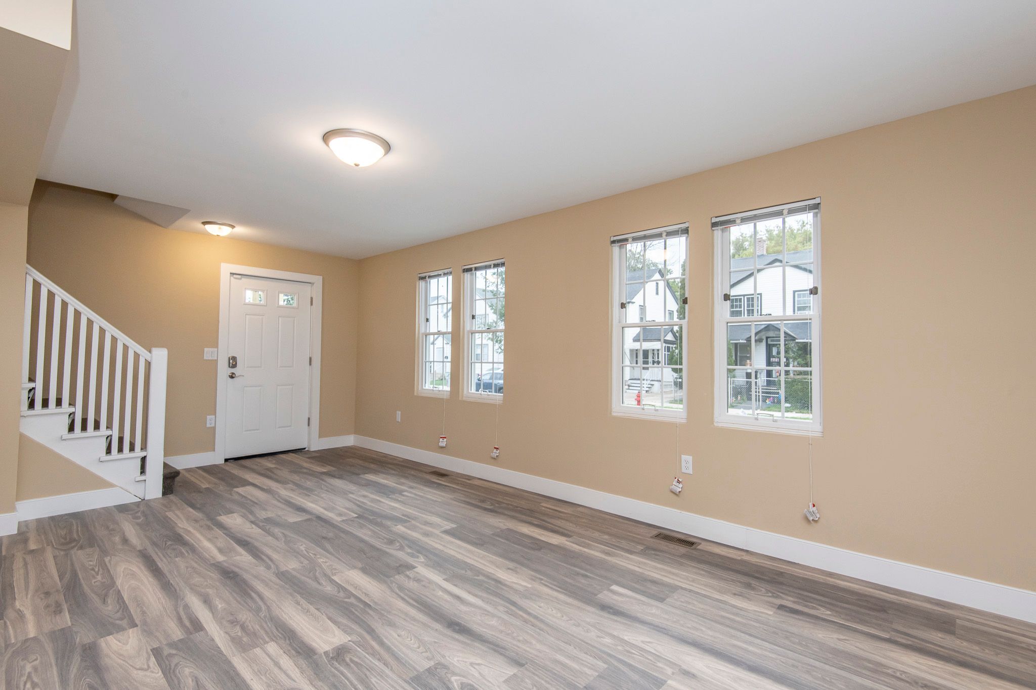 A room with a white door and two windows with a view of a house across the street.
