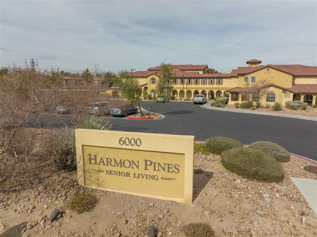 A sign for Harmon Pines Senior Living is in front of a building.