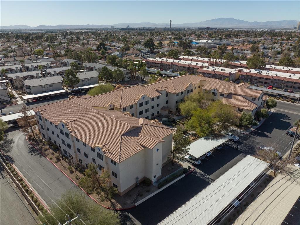 A large white building with a red tile roof is surrounded by a parking lot and other buildings.