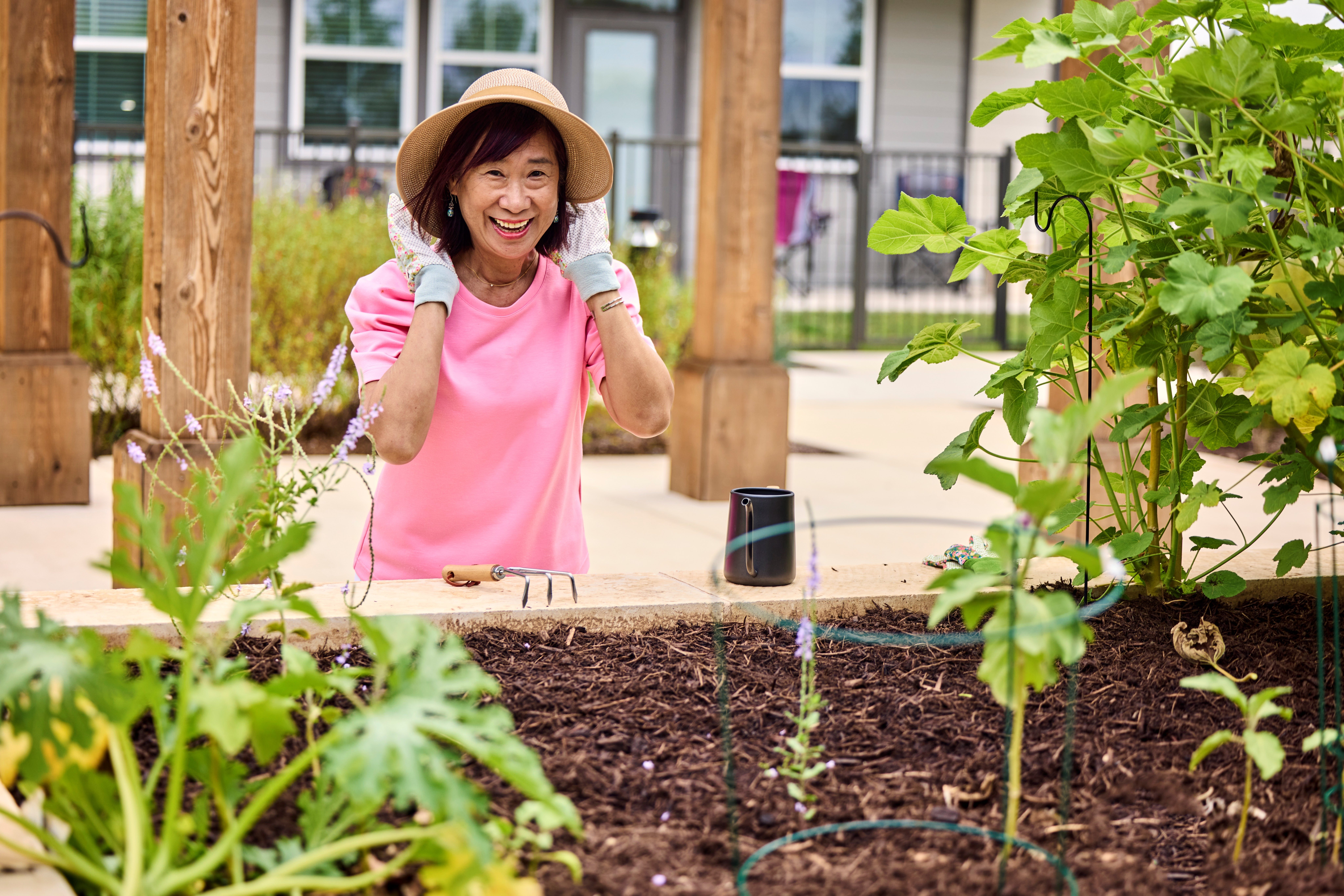 A woman in a pink shirt and hat is working in a garden.