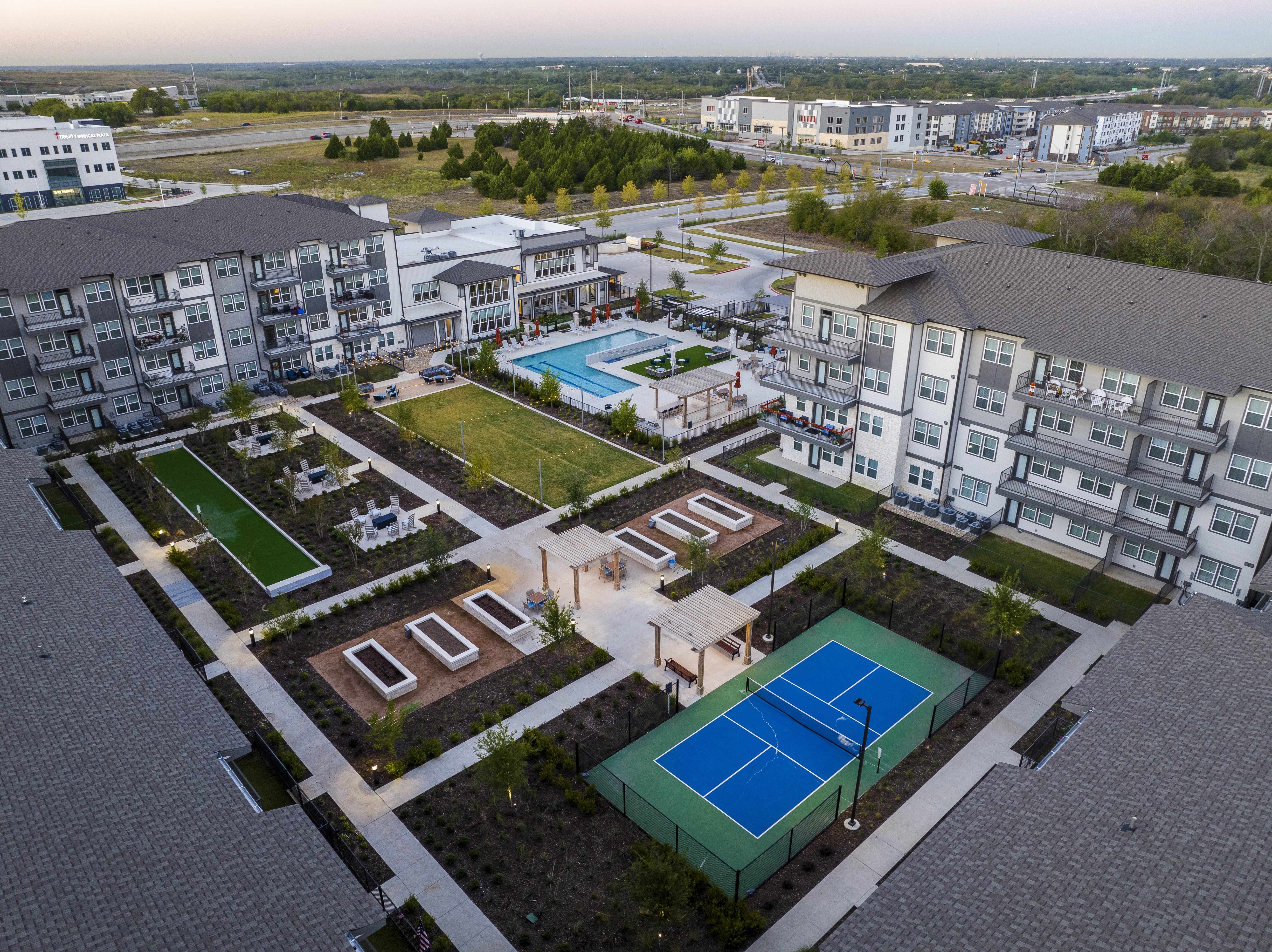 an aerial view of apartments with pickleball courts, bocce ball area, garden, and resort-style pool and courtyard at a senior apartment community
