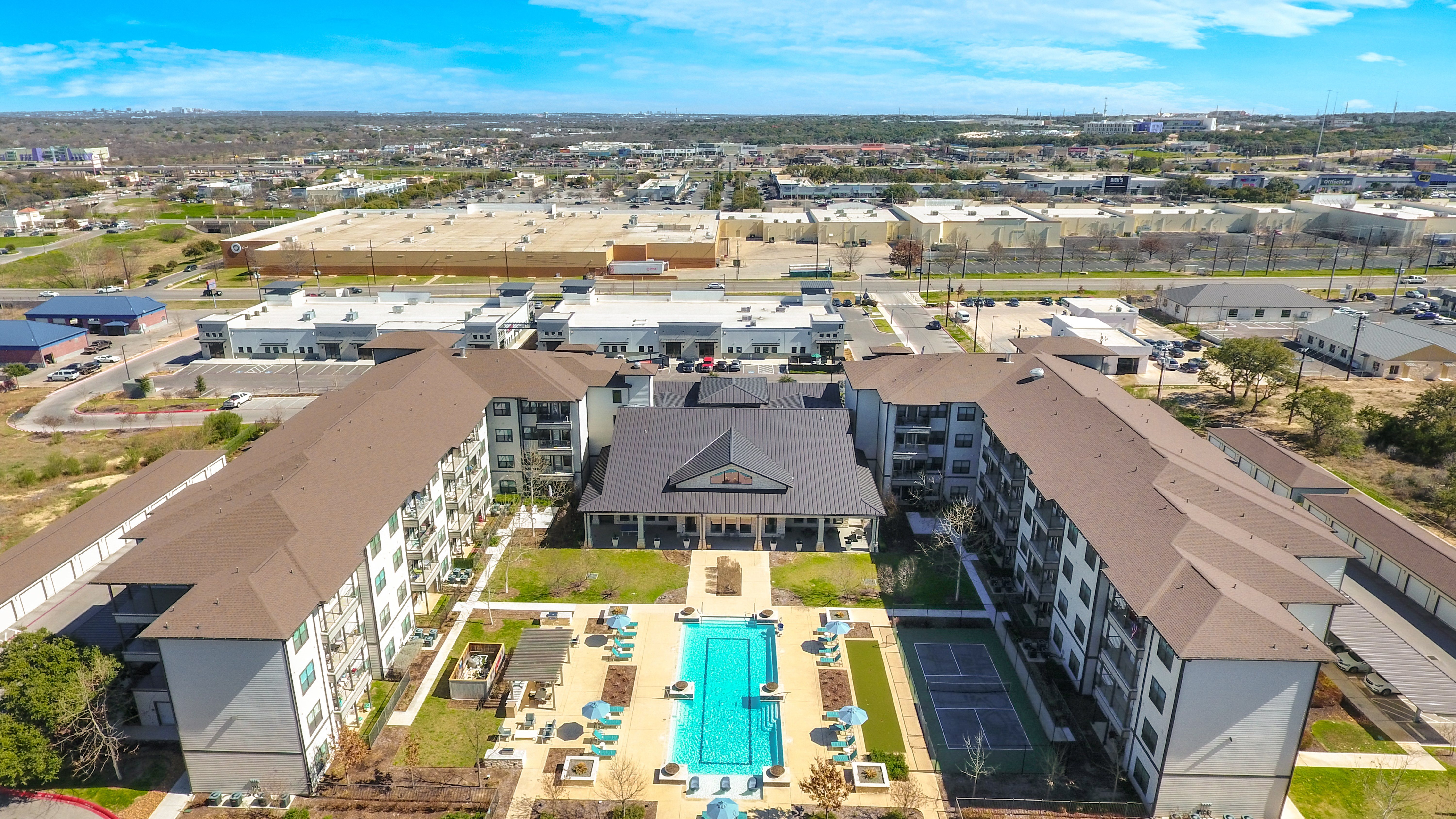 an aerial view of a resort-style pool, pickleball court, lawn, and courtyard at a senior apartment community
