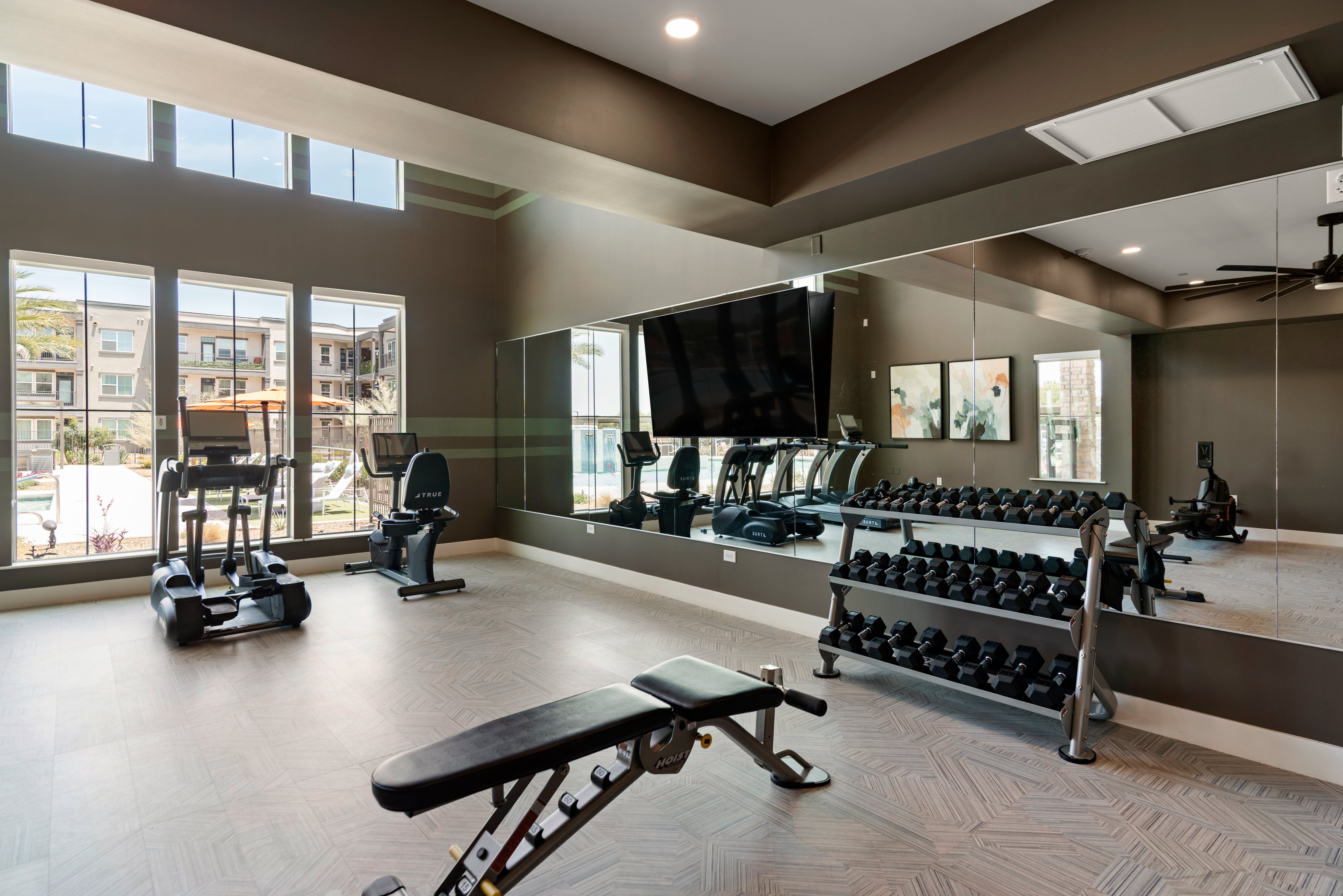 A gym with a variety of equipment including dumbbells, weight machines, and a flat screen TV.