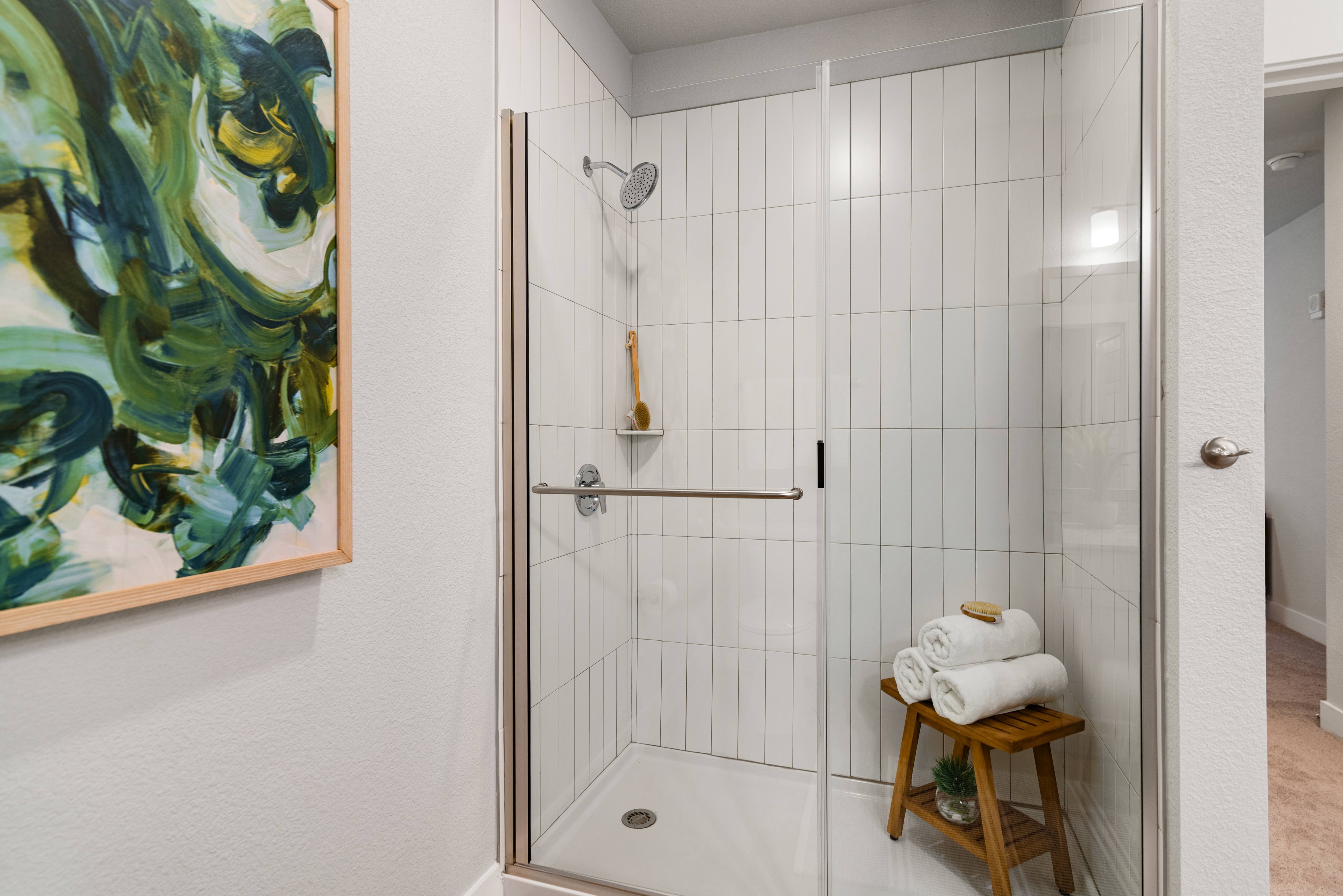 A bathroom with a glass shower stall and a painting on the wall.