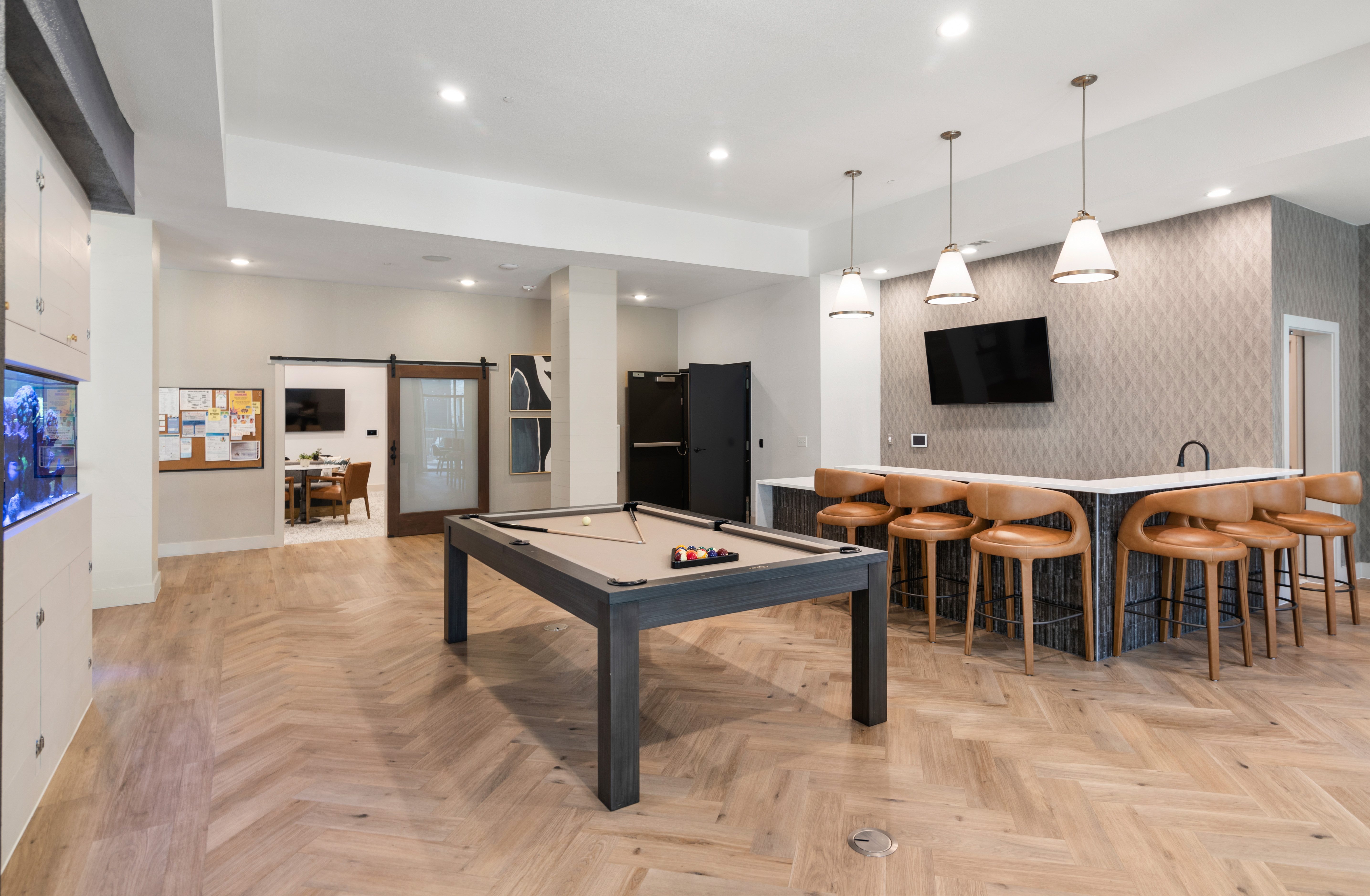 A billiard table is in the middle of a room with a bar and stools.