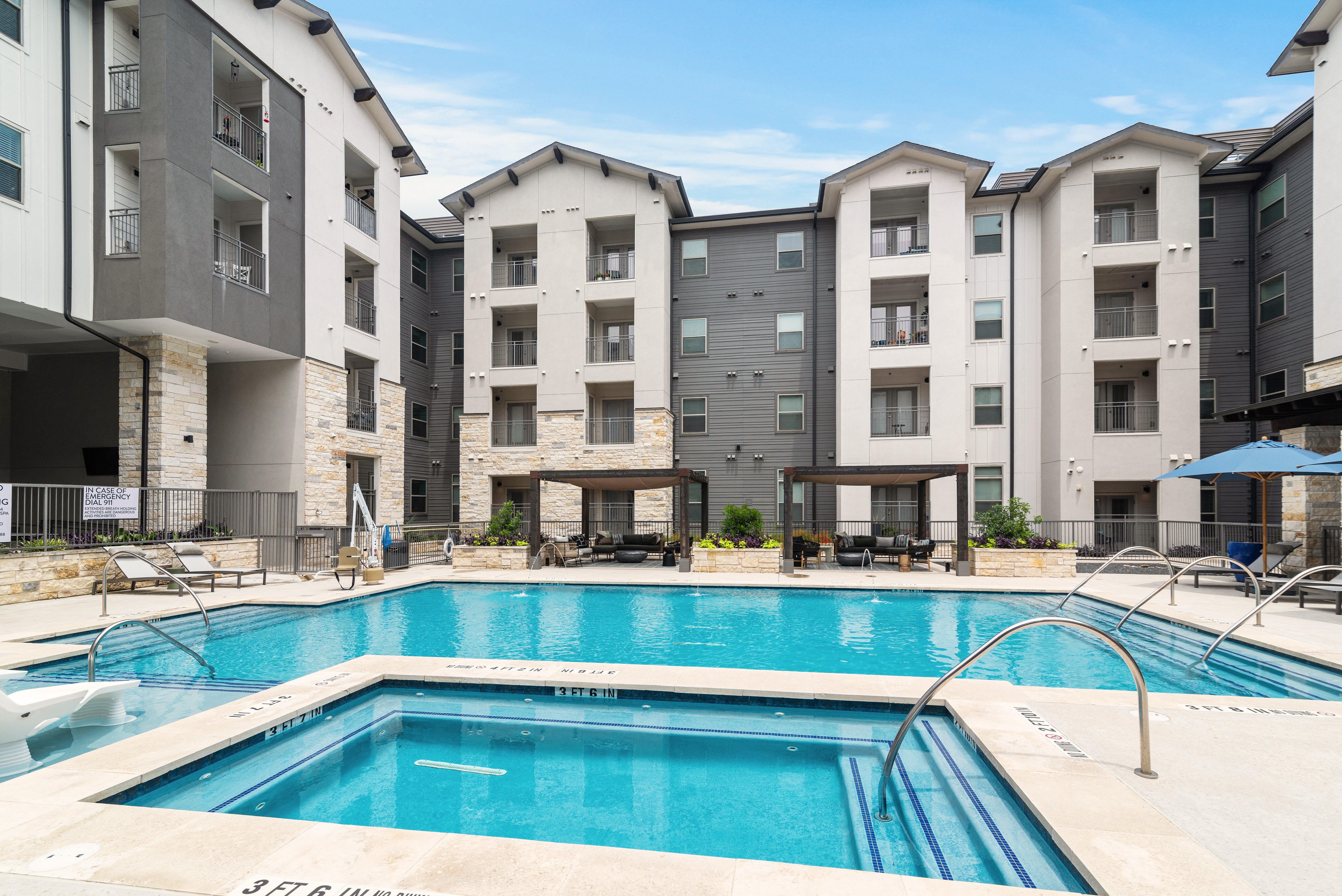 a resort-style swimming pool with sitting areas covered by a wooden pergola at a senior apartment community