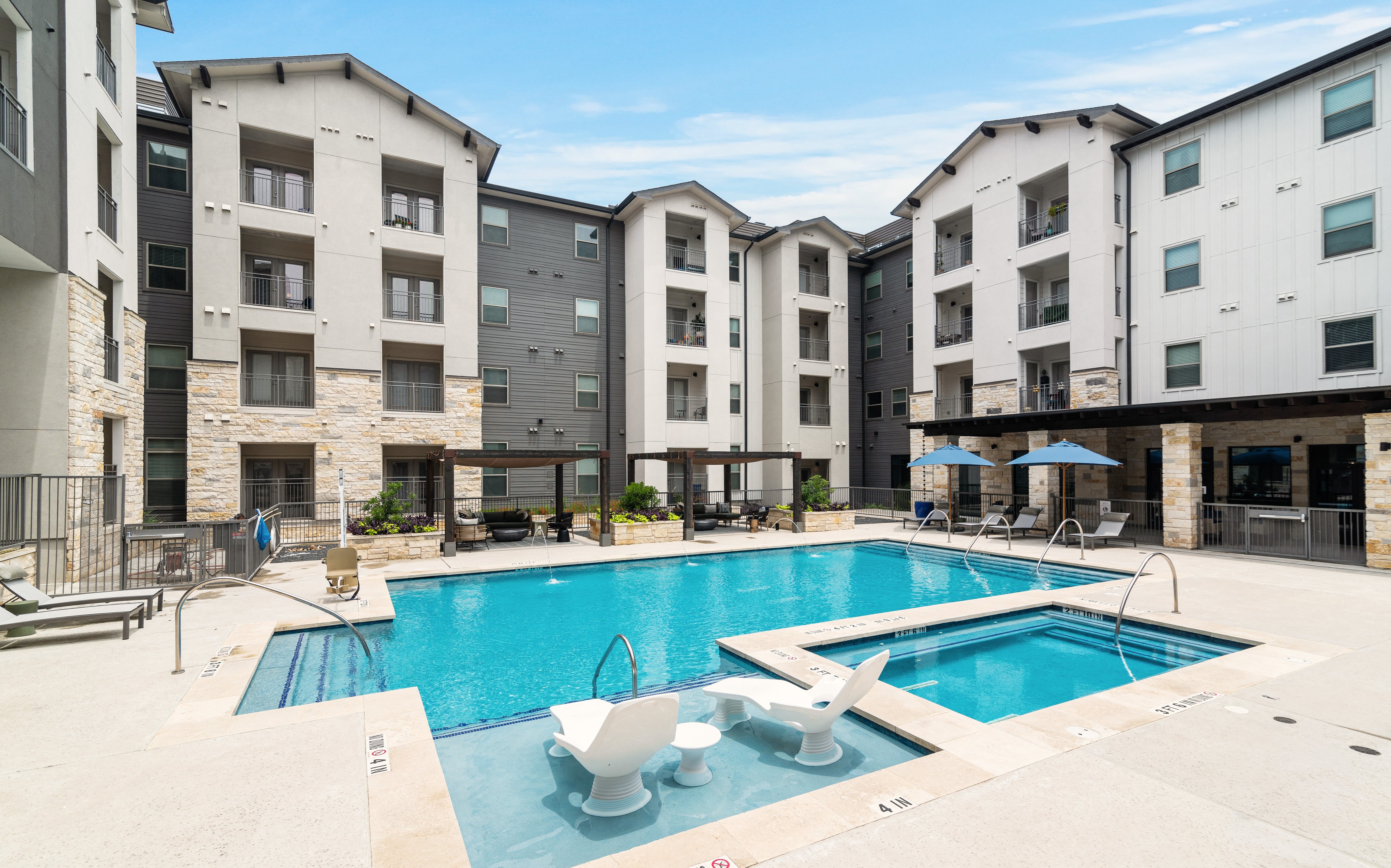 a resort-style swimming pool with lounge chairs and sitting areas covered by a wooden pergola at a senior apartment community