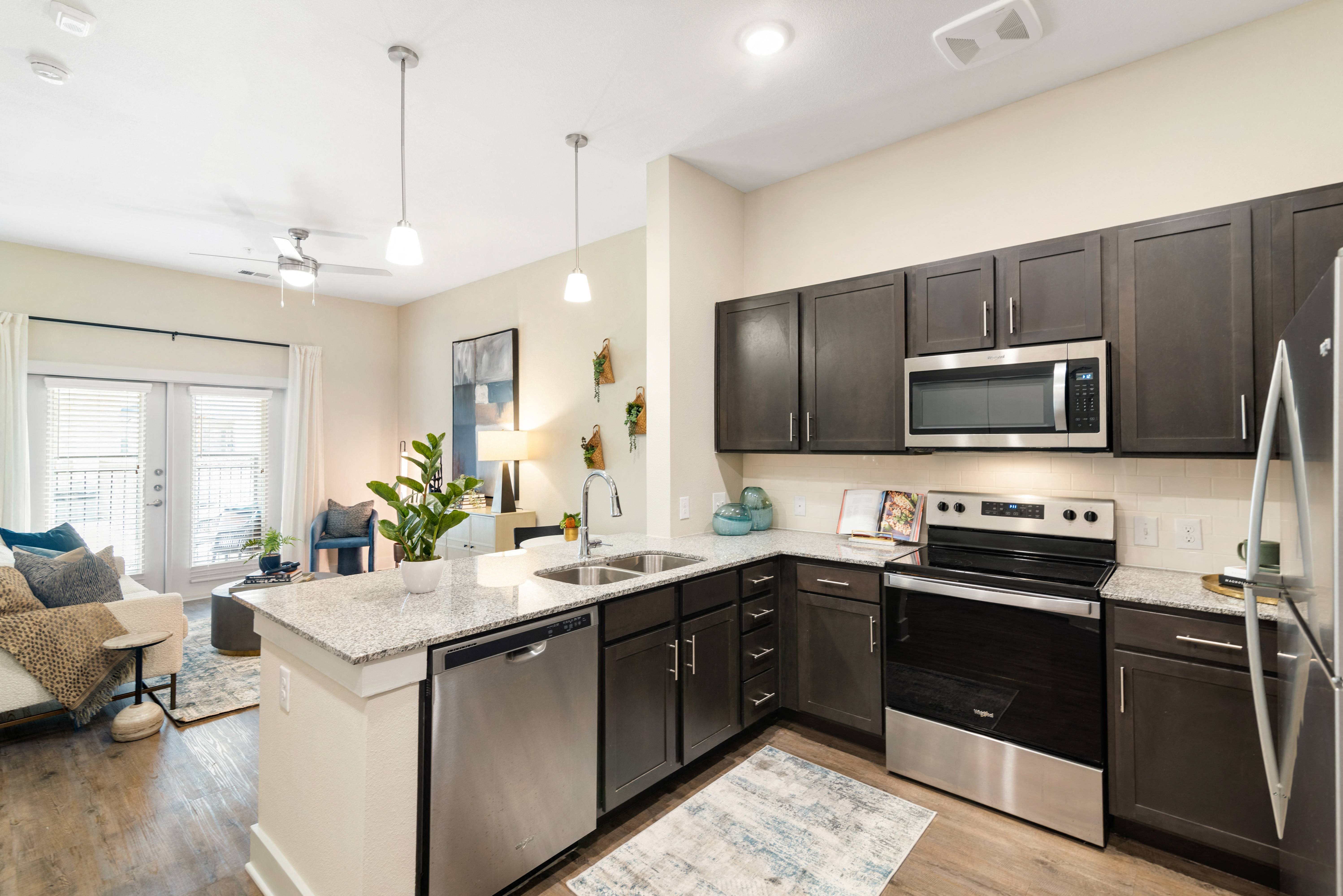 a kitchen with granite counter tops and stainless steel applicants with a view of a living room and patio at a senior apartment community