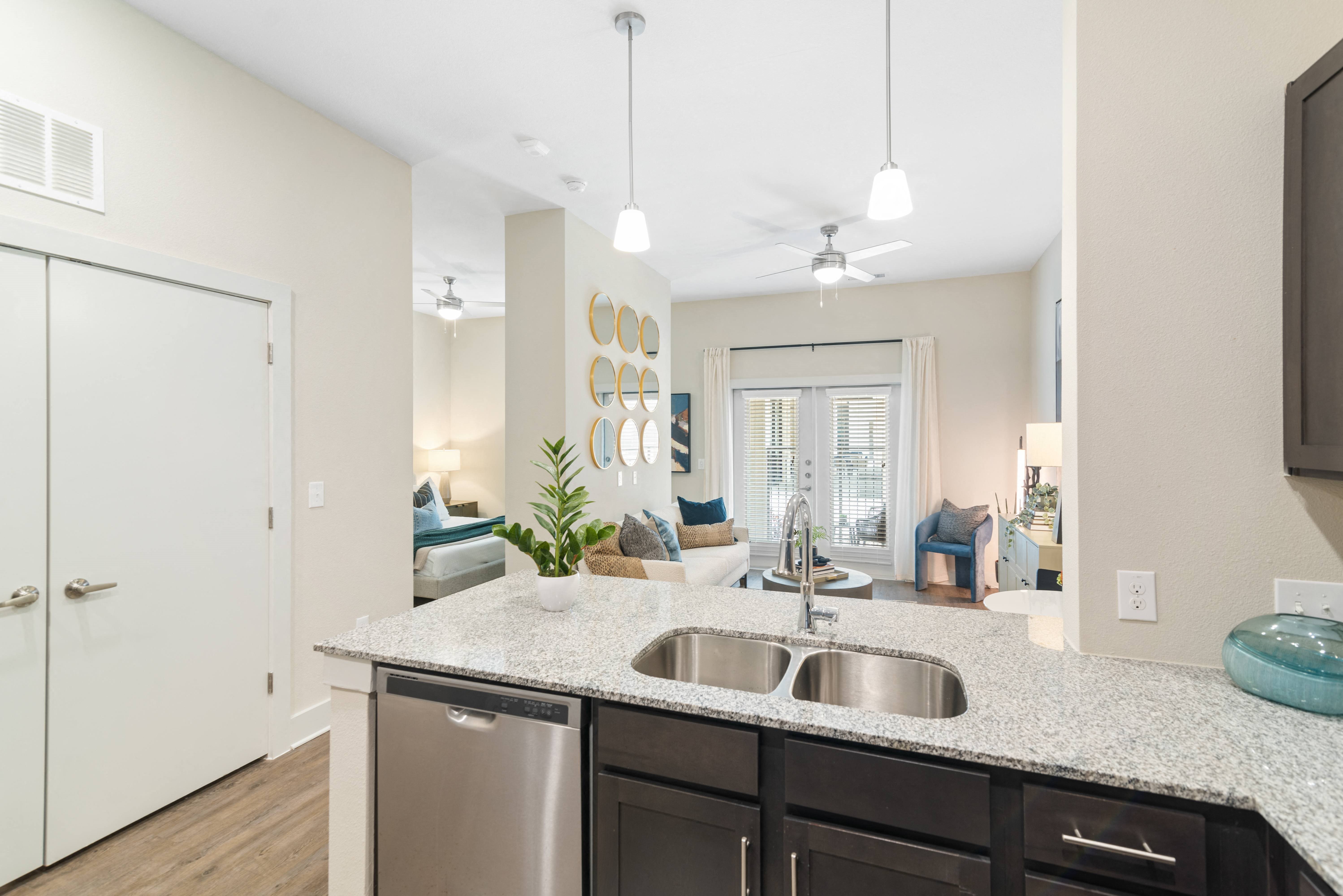 a kitchen with granite counter tops and stainless steel appliances with a view of a living room and patio at a senior apartment community