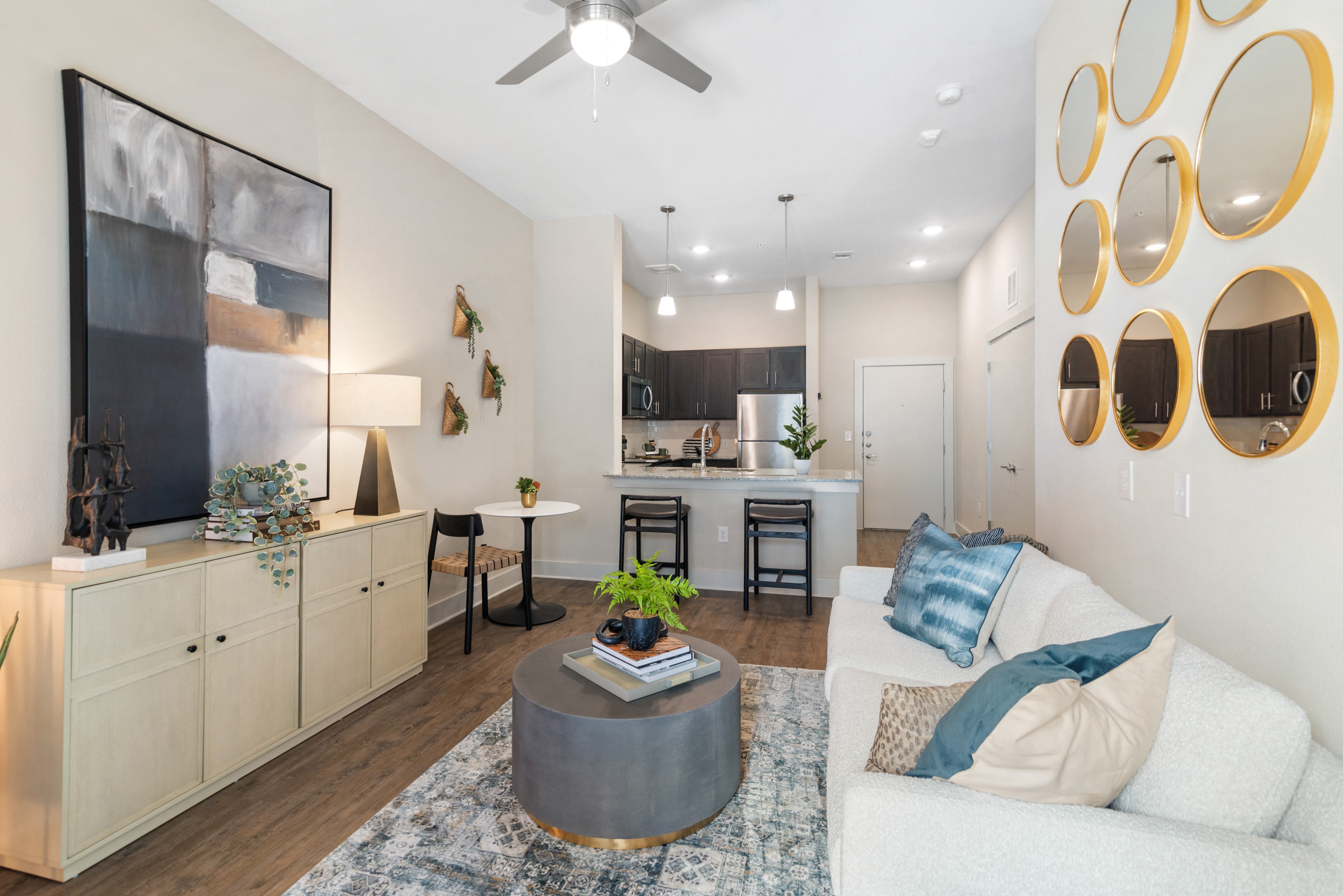 a living room with a ceiling fan with a view of a kitchen at a senior apartment community