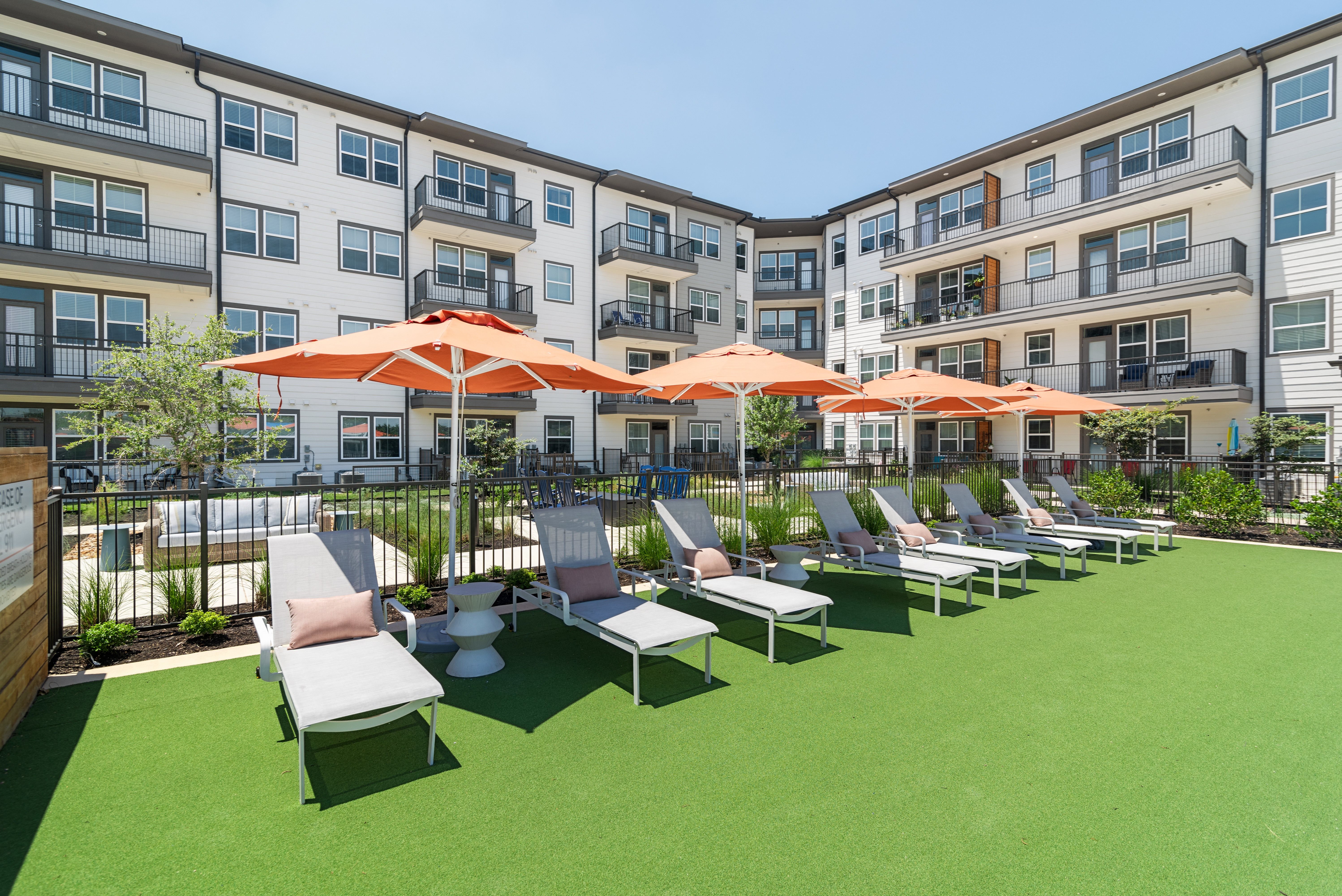 an outdoor lounge area with chairs and umbrellas in front of an apartment building