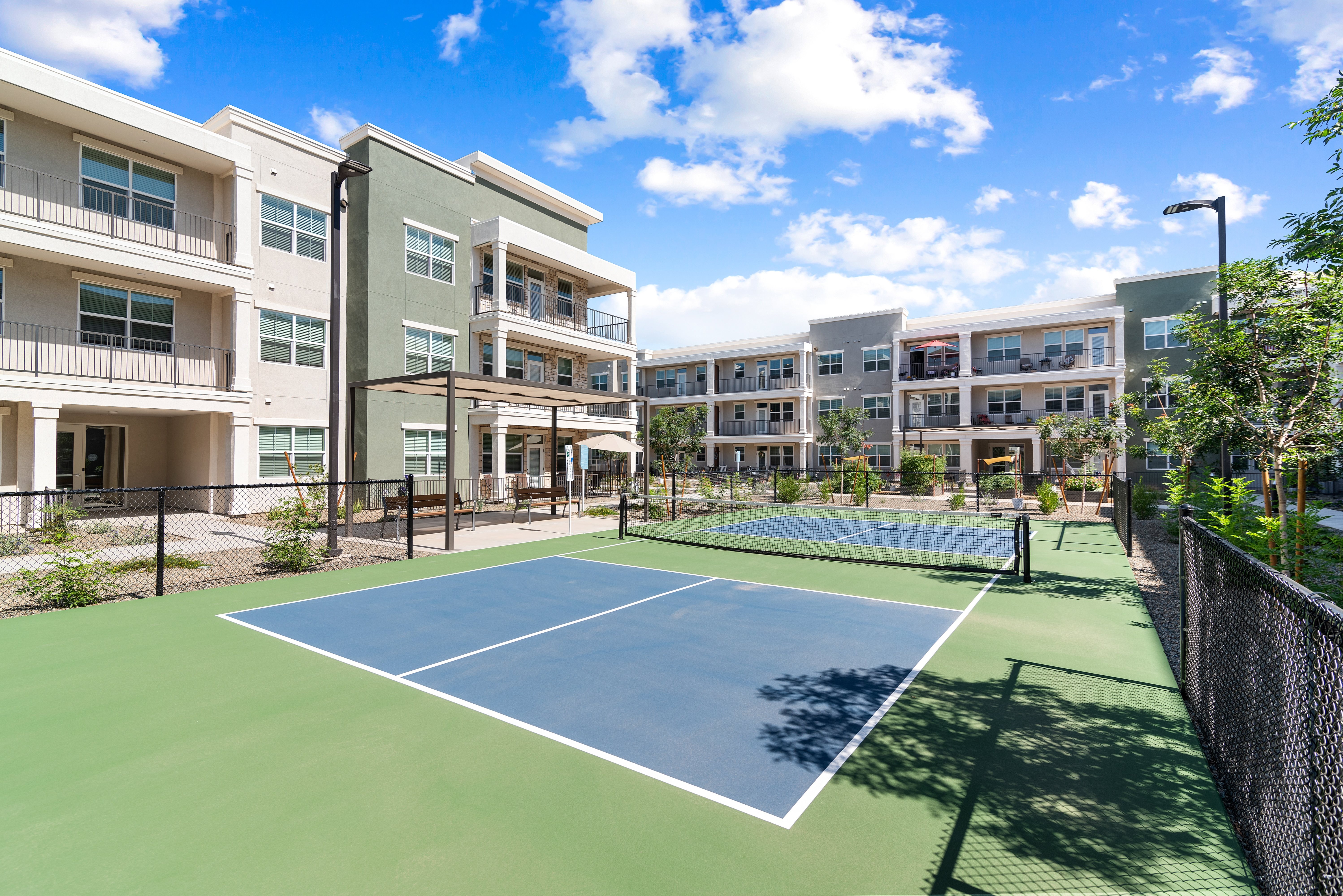 A tennis court is surrounded by apartment buildings.