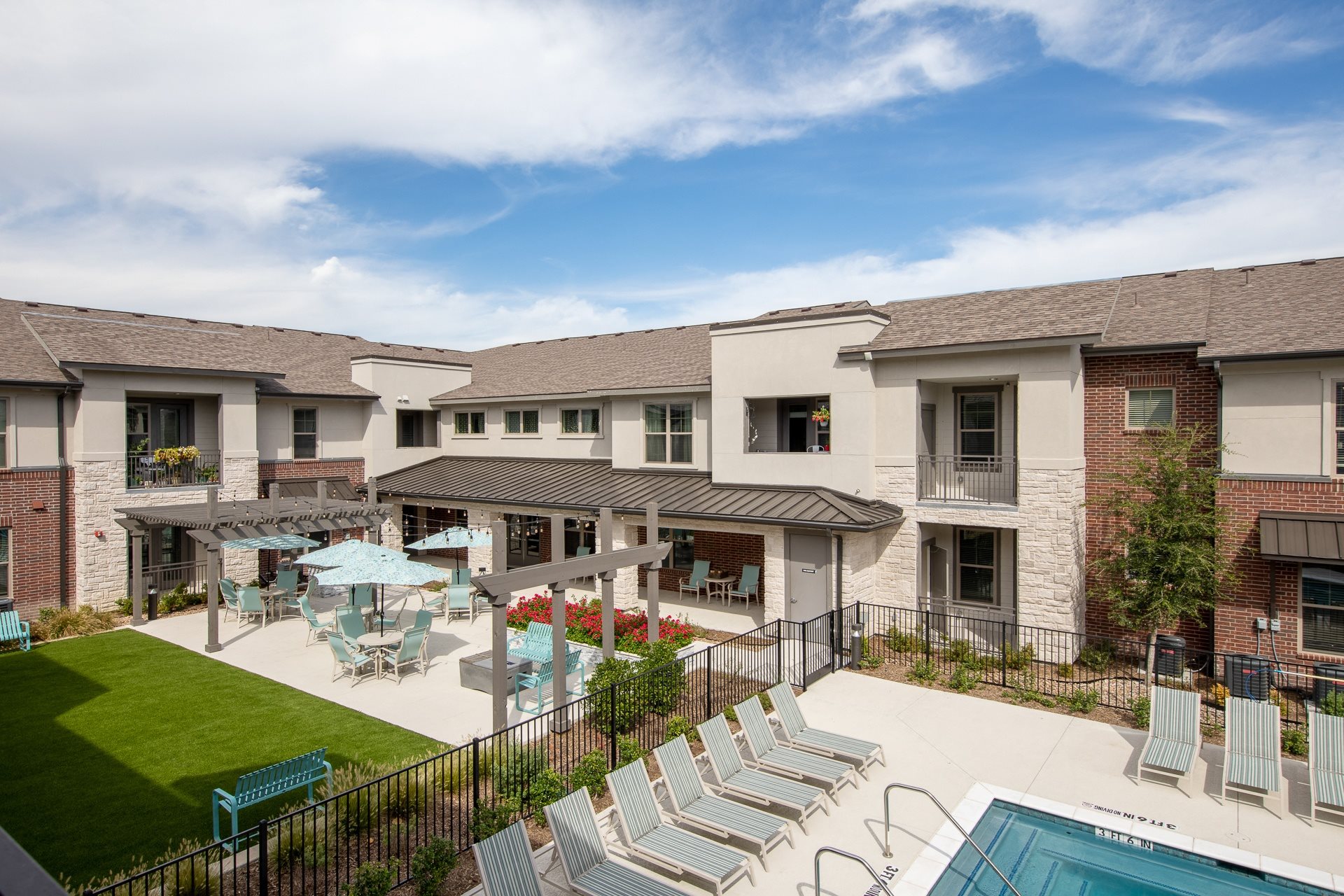 a resort-style pool with lounge chairs and patio seating under umbrellas at a senior apartment community
