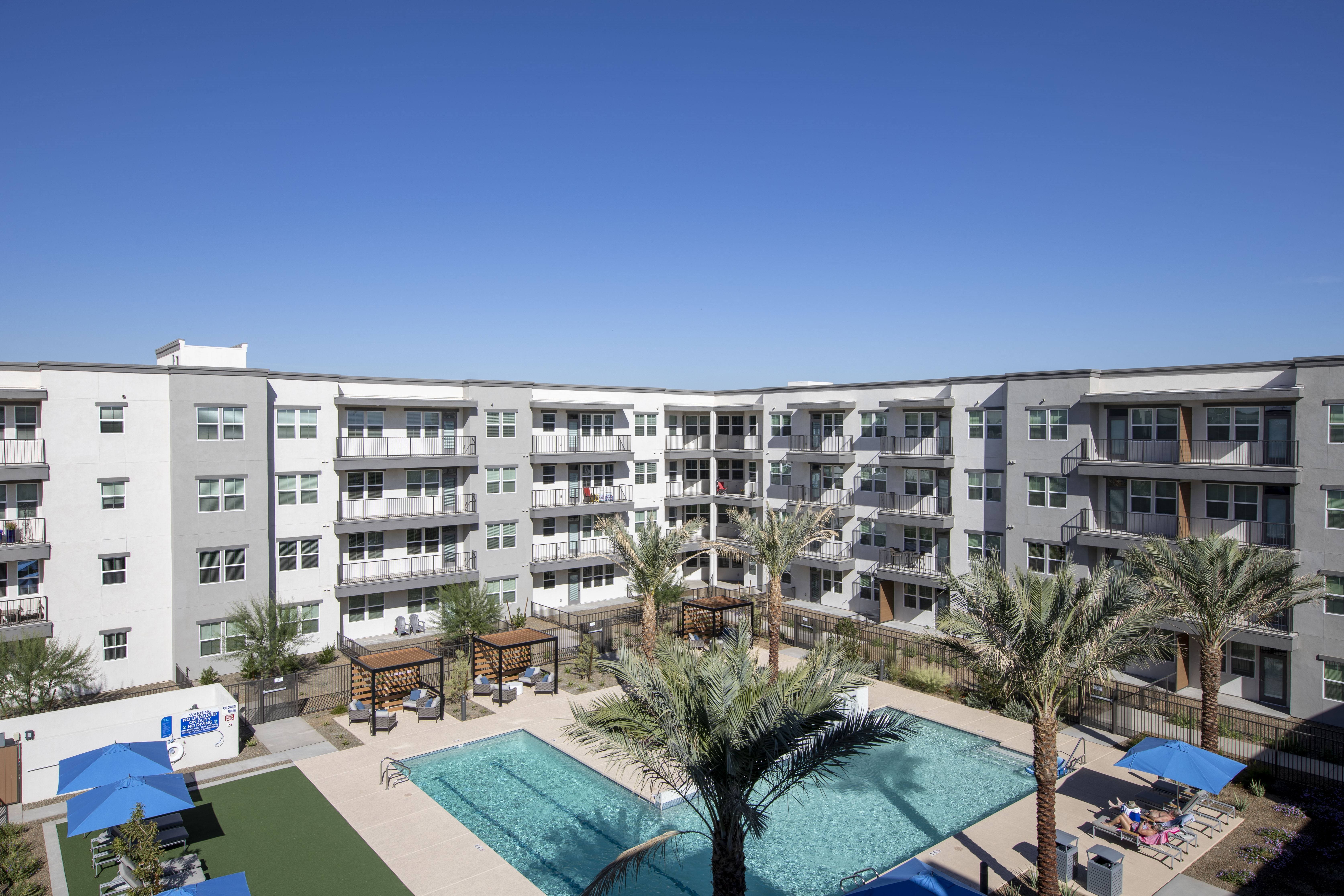 an aerial view of a resort-style pool and covered sitting lounge areas at a senior apartment community