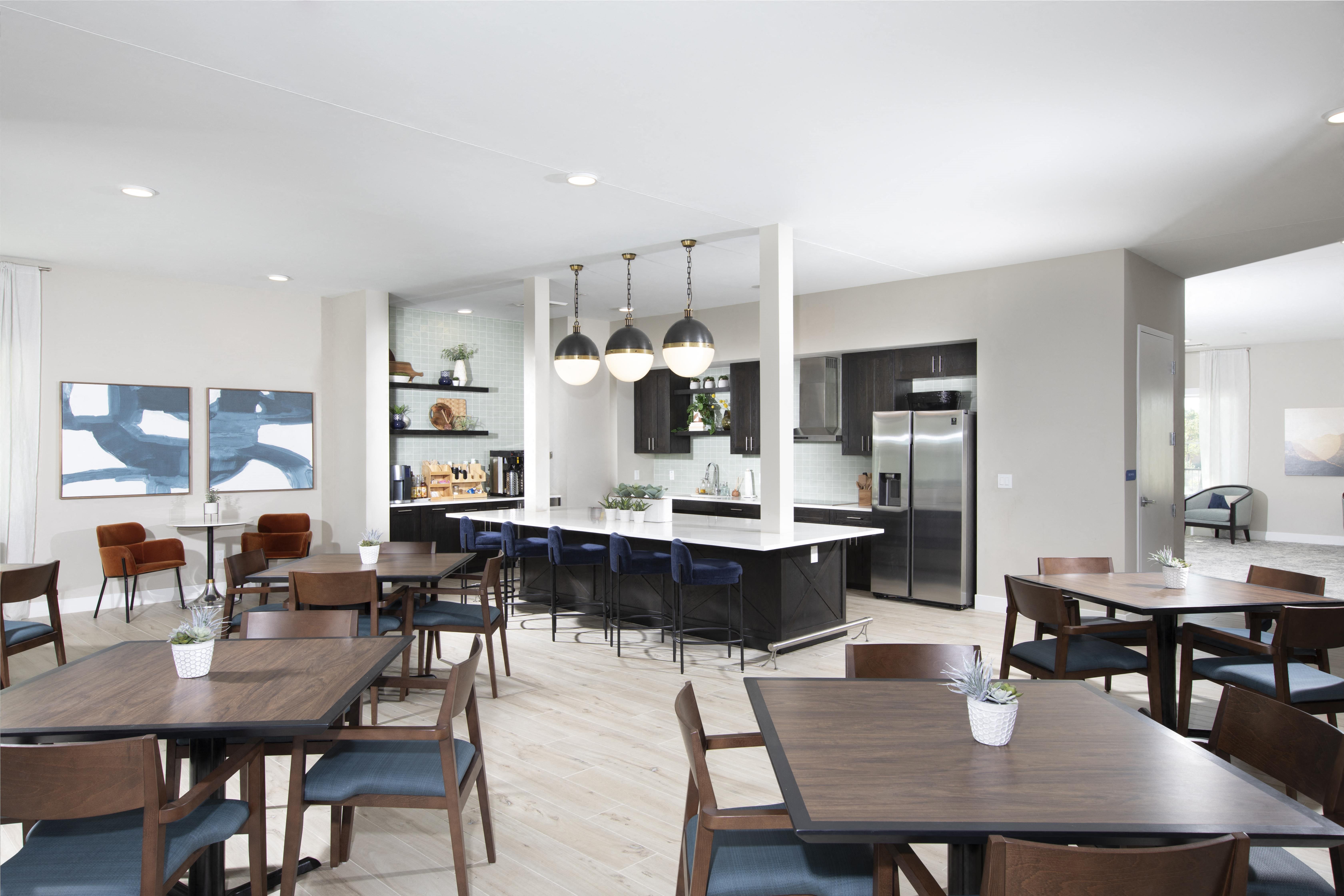 an open concept, communal kitchen and dining room with tables and chairs at a senior apartment community