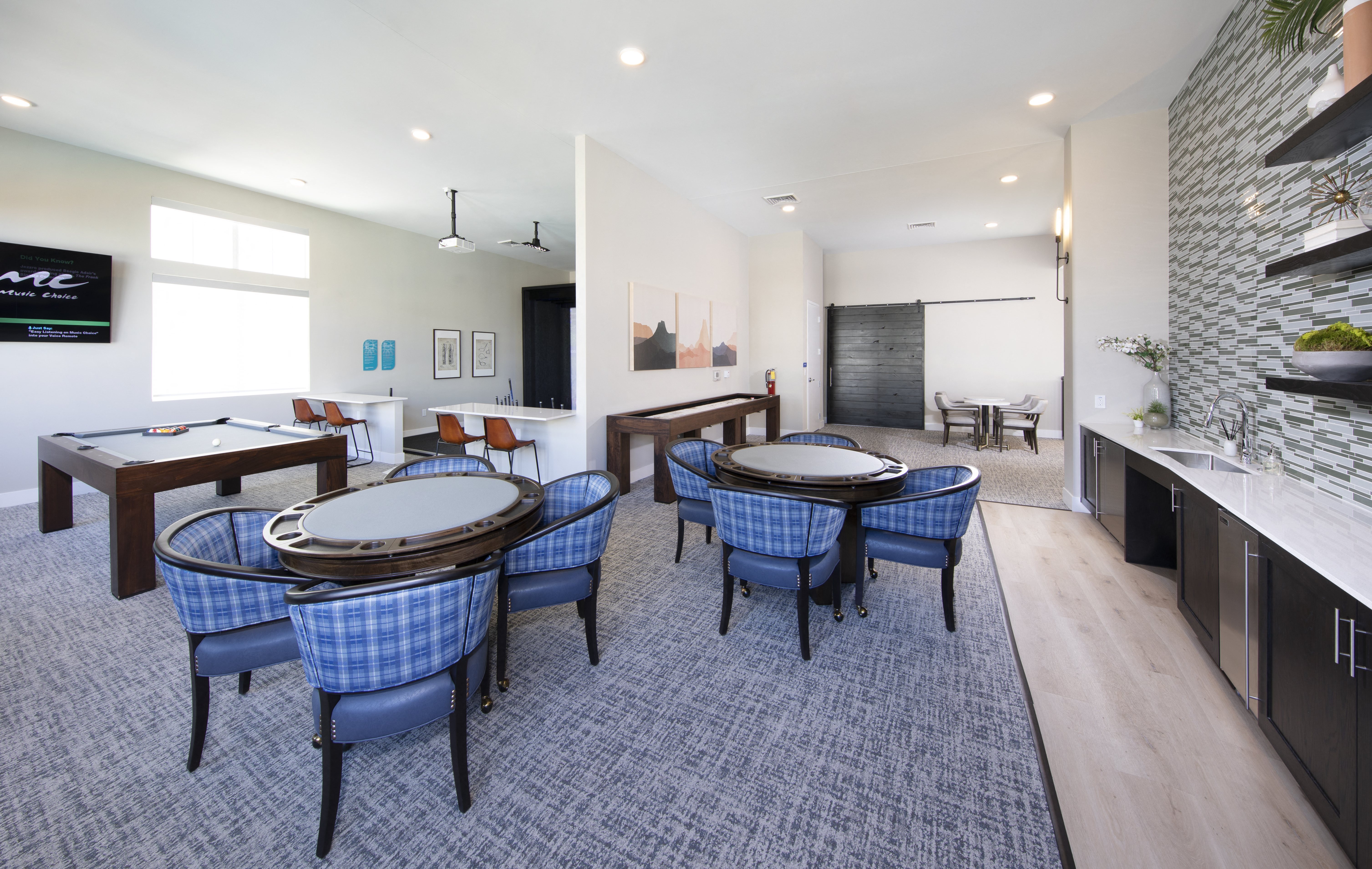 a game room with a golf simulator, pool table, and card tables with chairs at a senior apartment community