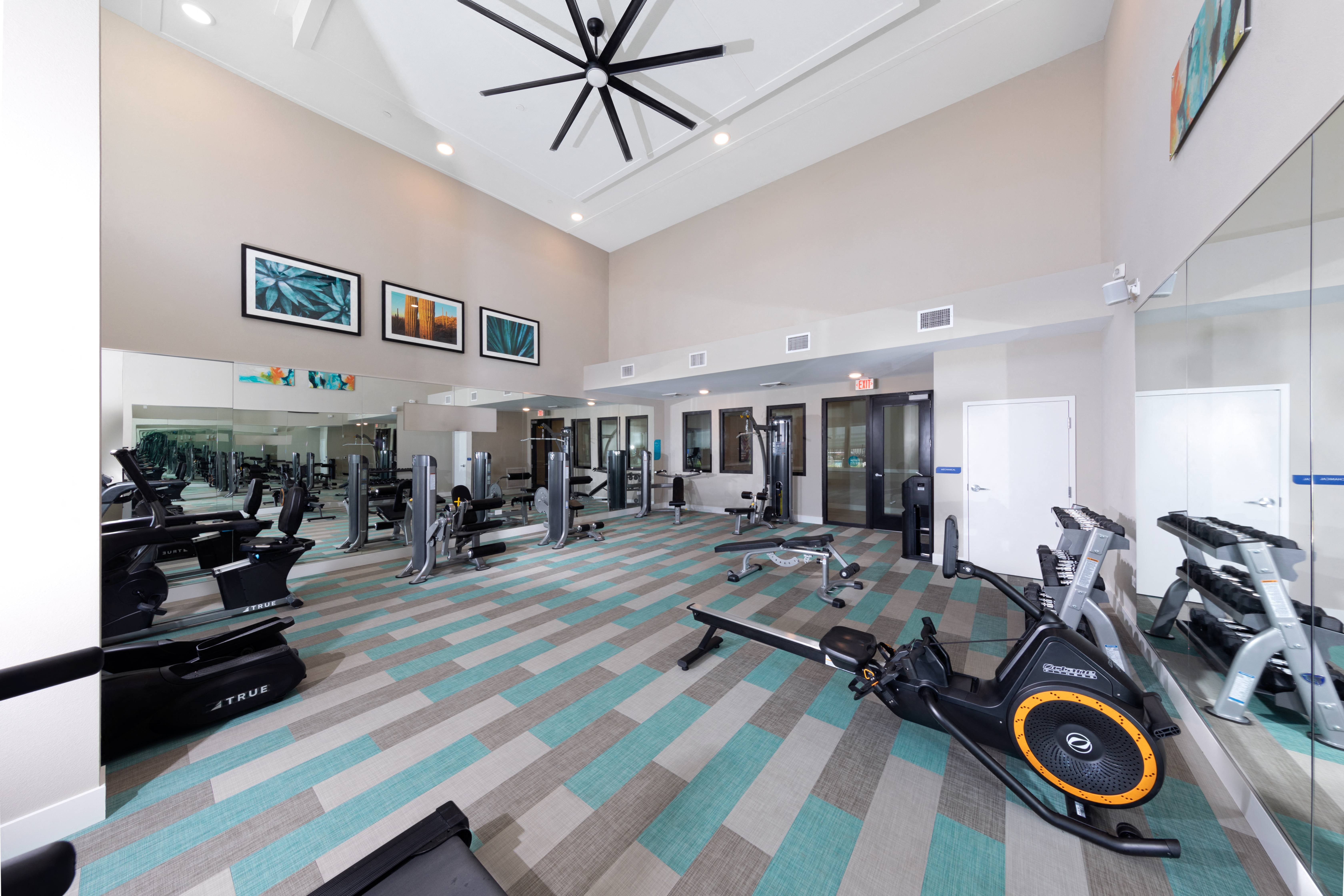a gym with workout machines and equipment and a large ceiling fan at a senior apartment community