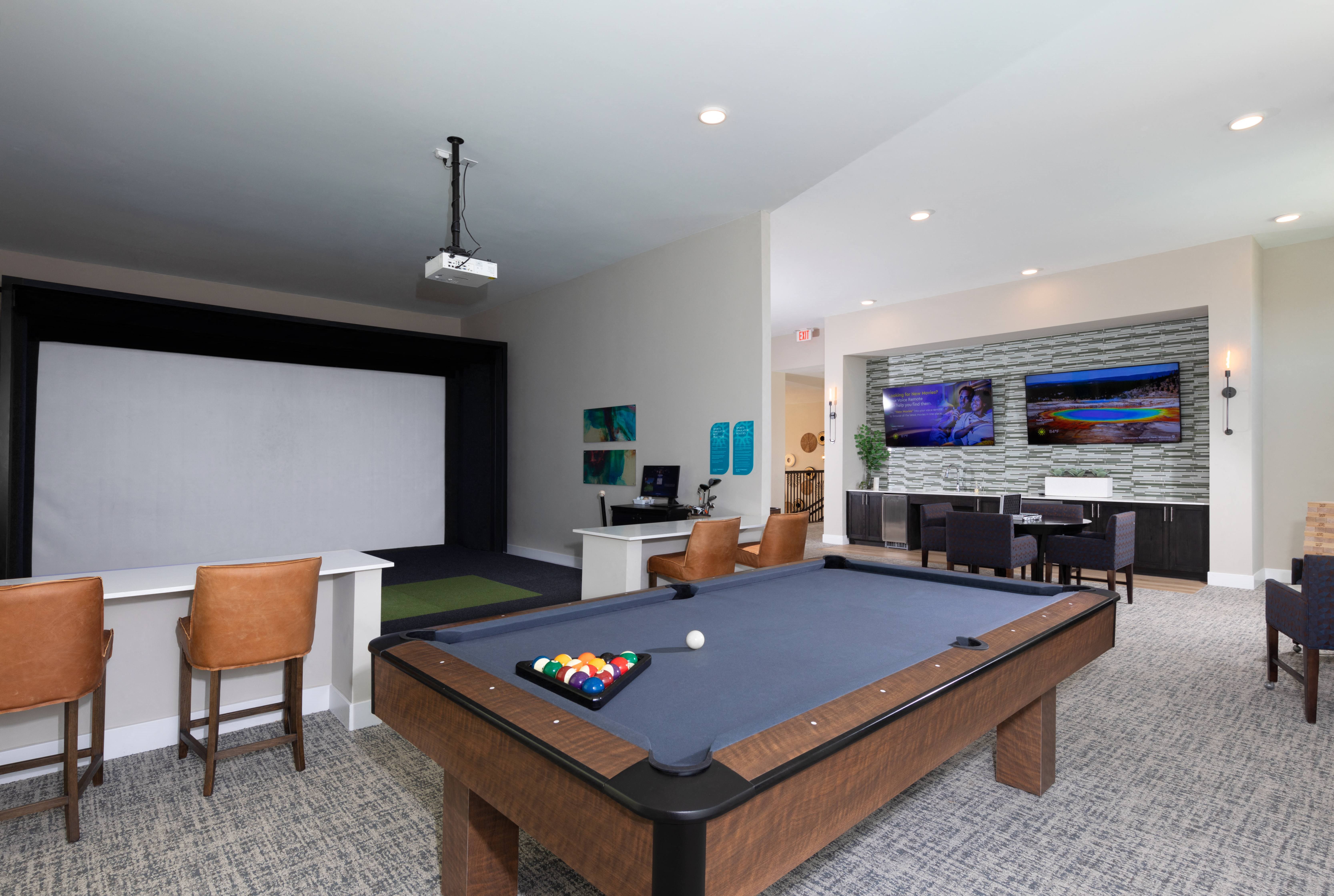 a game room with a pool table, golf simulator, and sitting areas at a senior apartment community