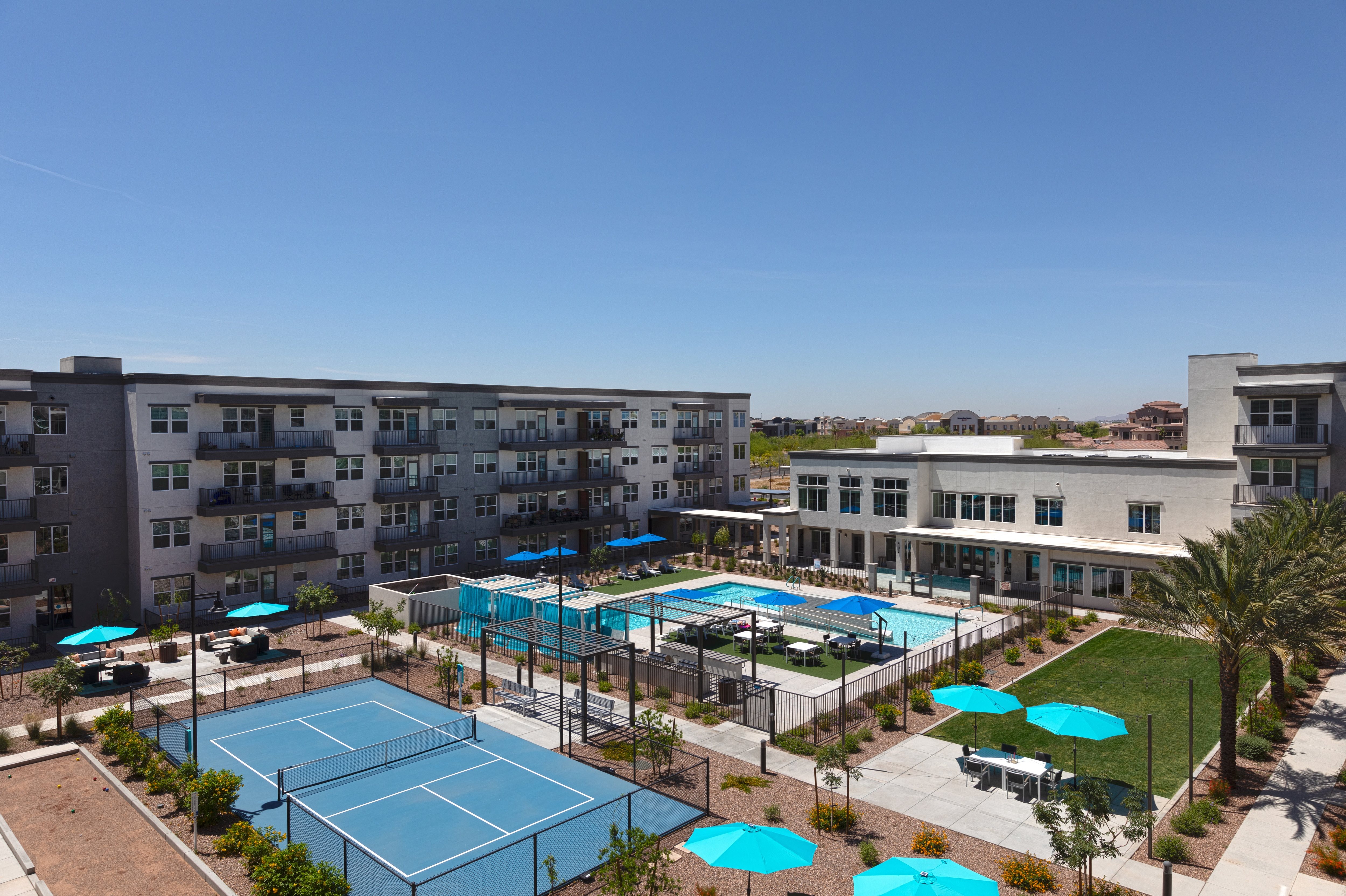 an aerial view of a resort-style pool, and patio areas, pickleball court, and lawn at a senior apartment community