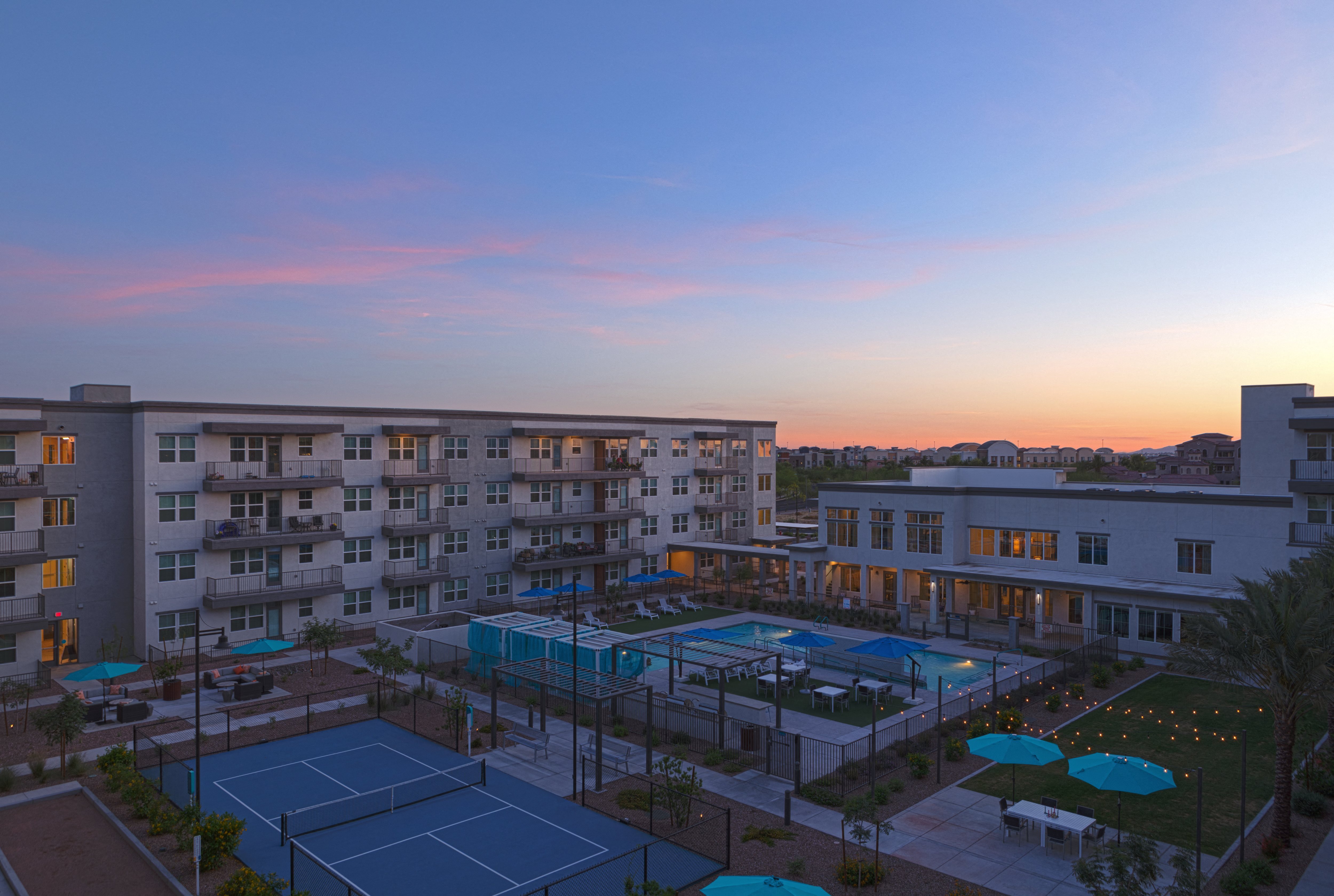 an aerial view of a pickleball court, resort-style pool and patio area, bocce ball court, and lawn at a senior apartment community