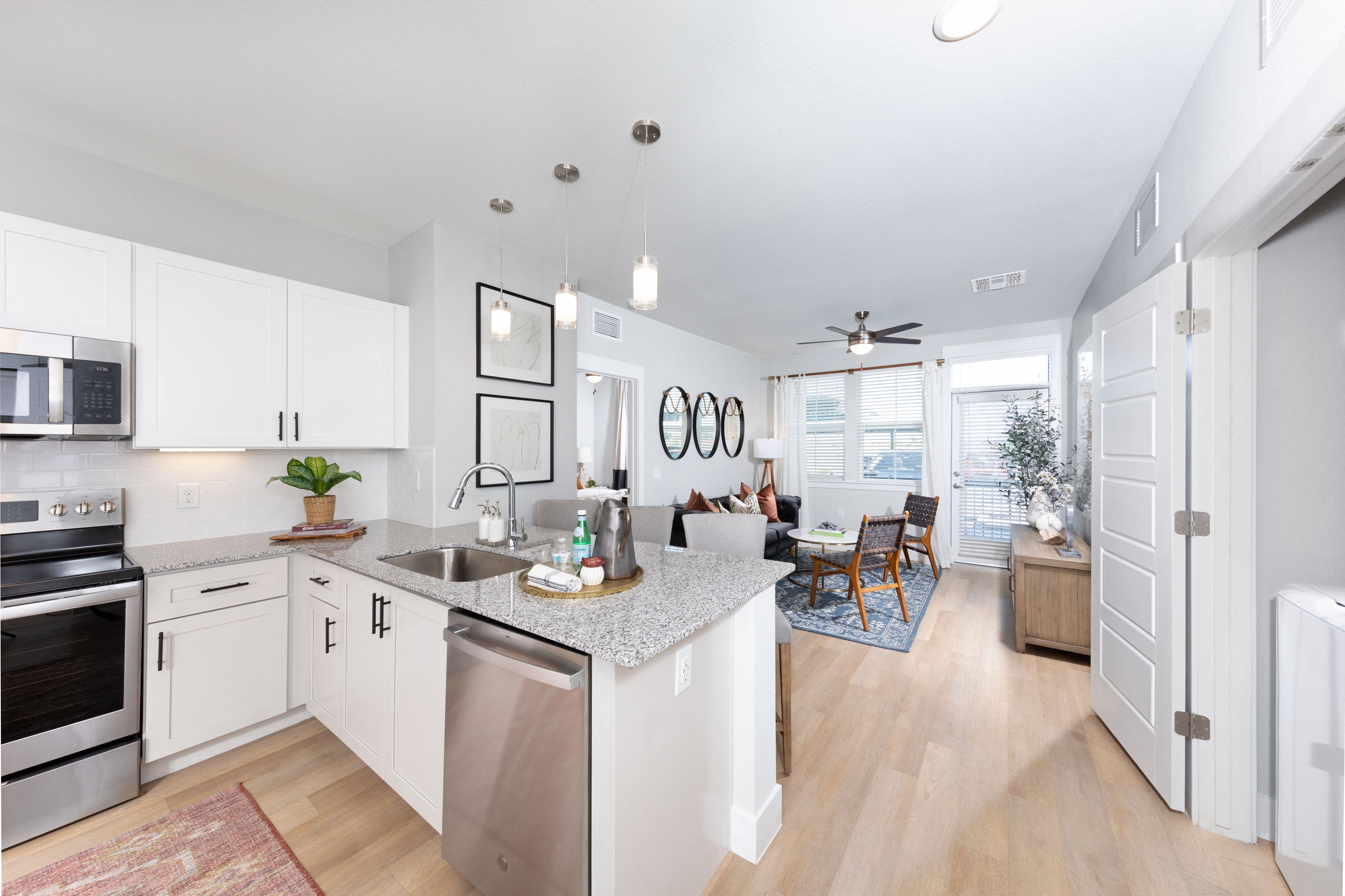 a kitchen with stainless steel appliances and granite countertops opening up to a living room at a senior apartment community