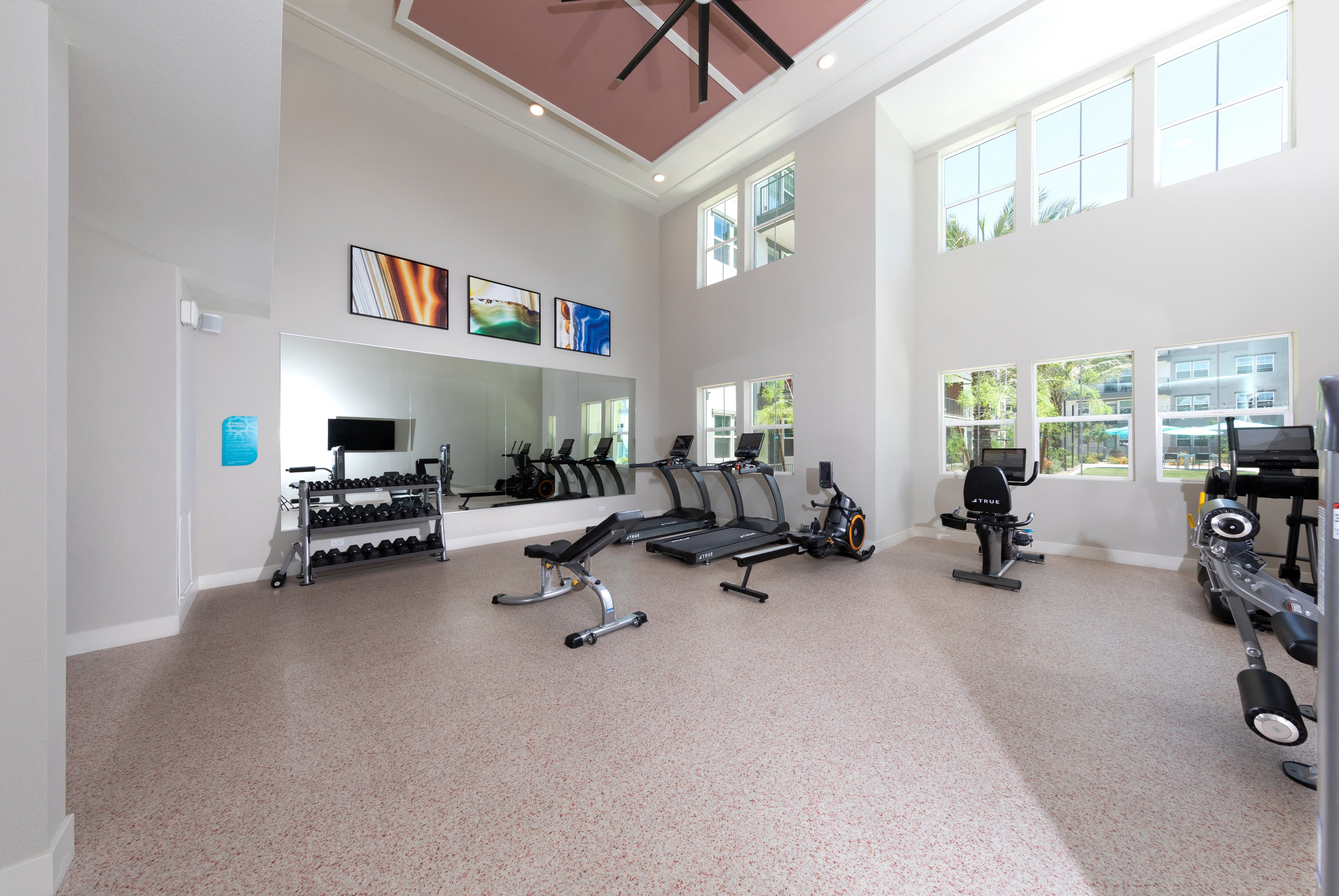 a gym with fitness equipment and machines and a large ceiling fan at a senior apartment community