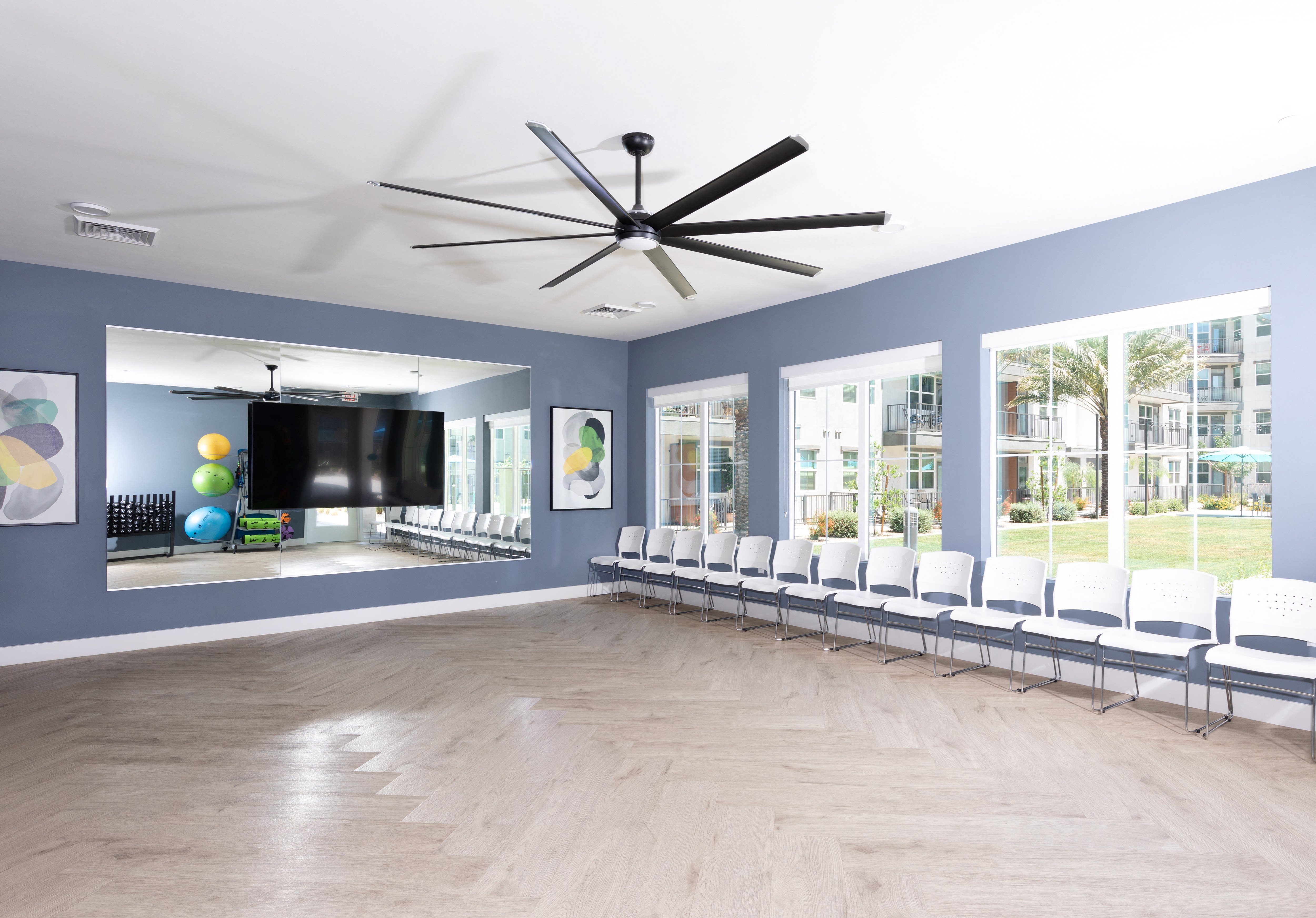 a fitness room with a large ceiling fan and mirrors at a senior apartment community