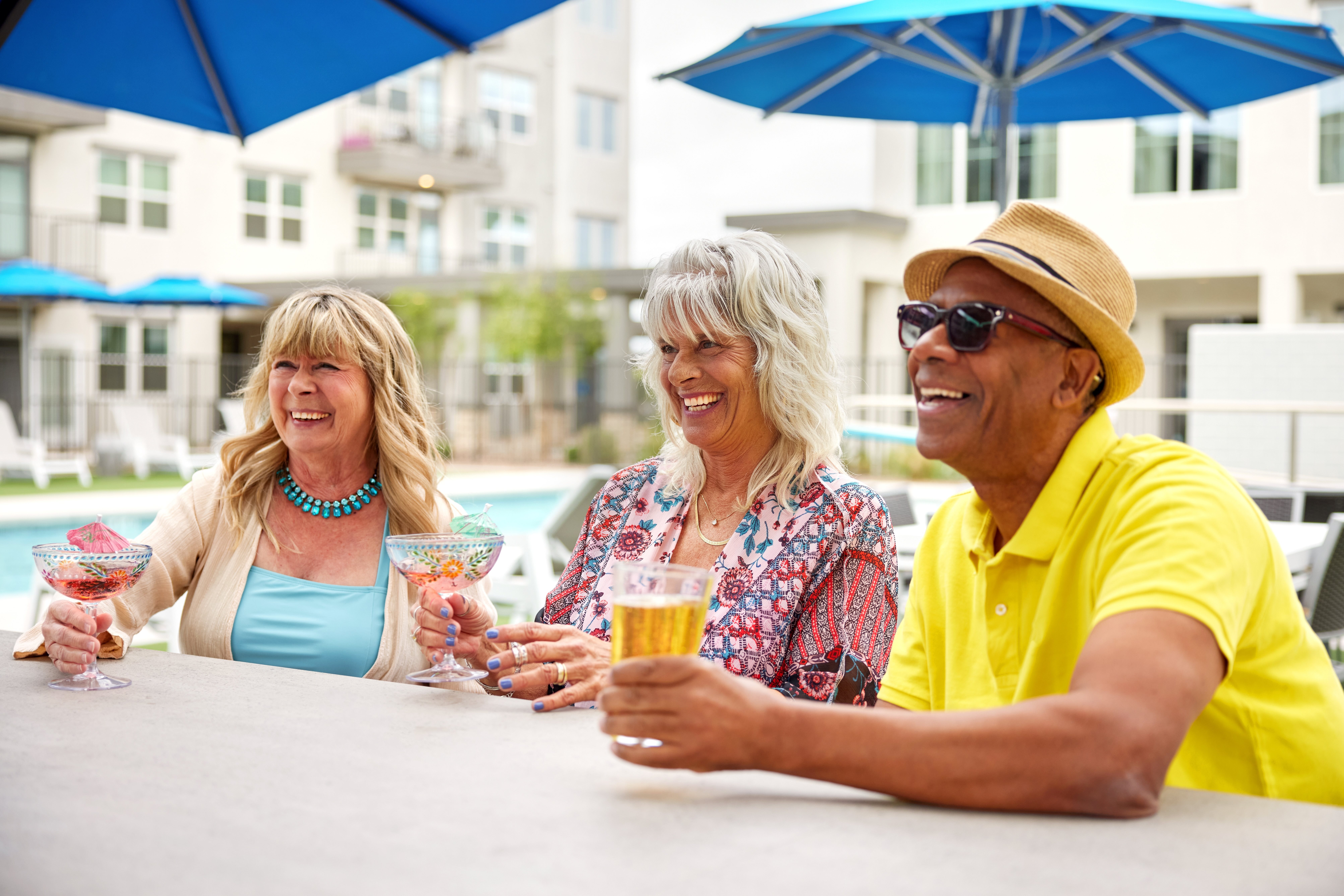 Three people are sitting at a table with drinks in front of a pool.