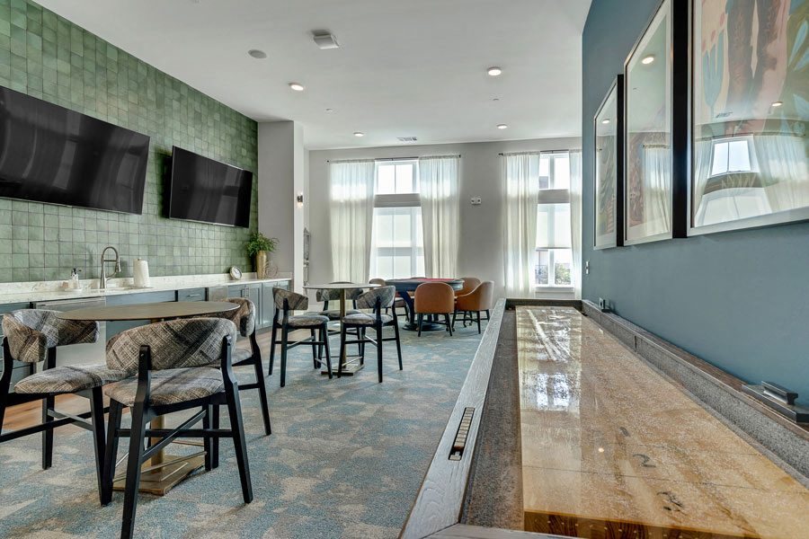 a game room with a table shuffleboard, card tables and chairs, and a television at a senior apartment community