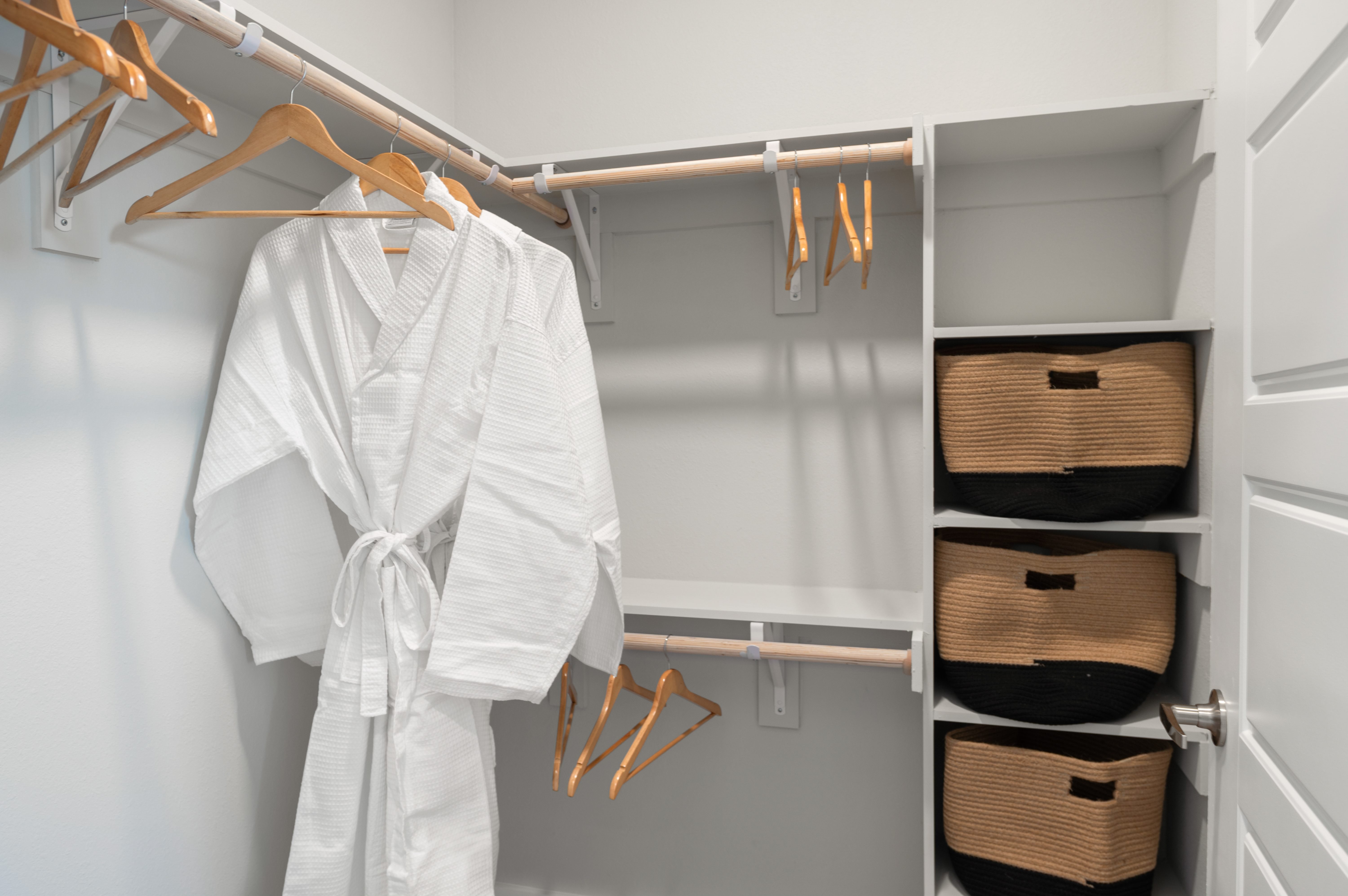 A white robe is hanging on a rack in a closet with baskets underneath.
