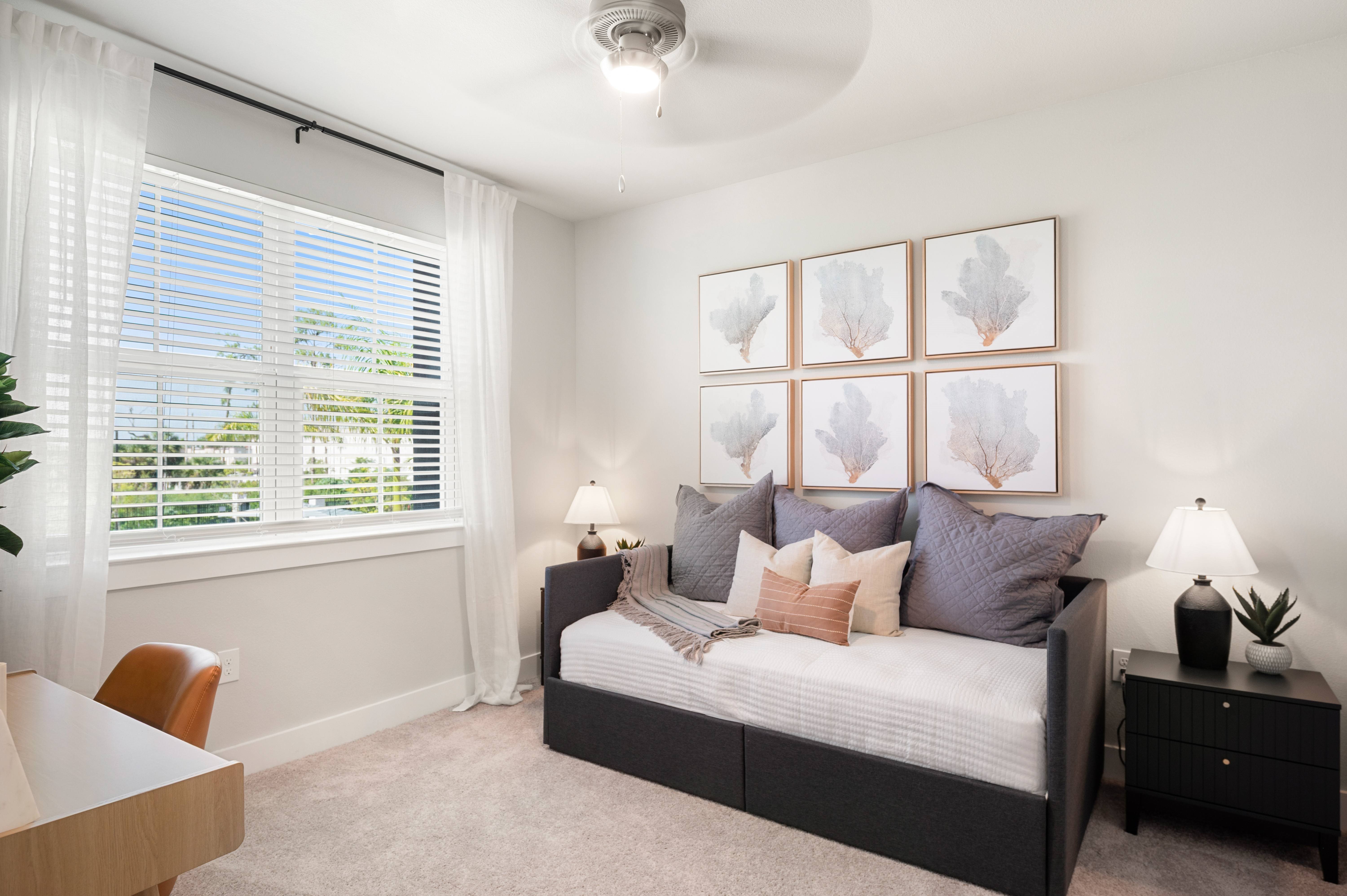 A bedroom with a bed, a chair, a plant, and a painting on the wall.