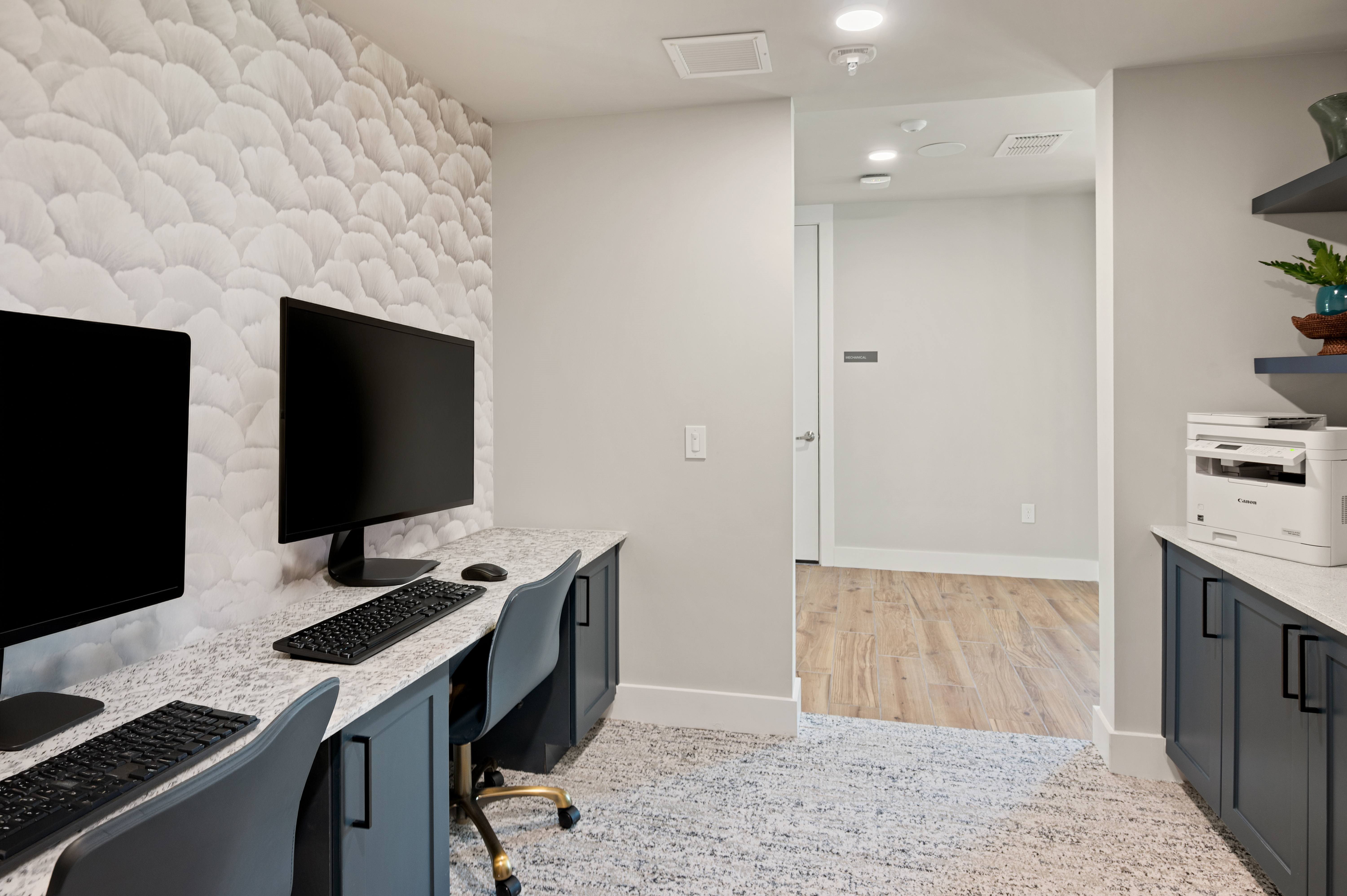 A home office with a desk, chairs, and two monitors.