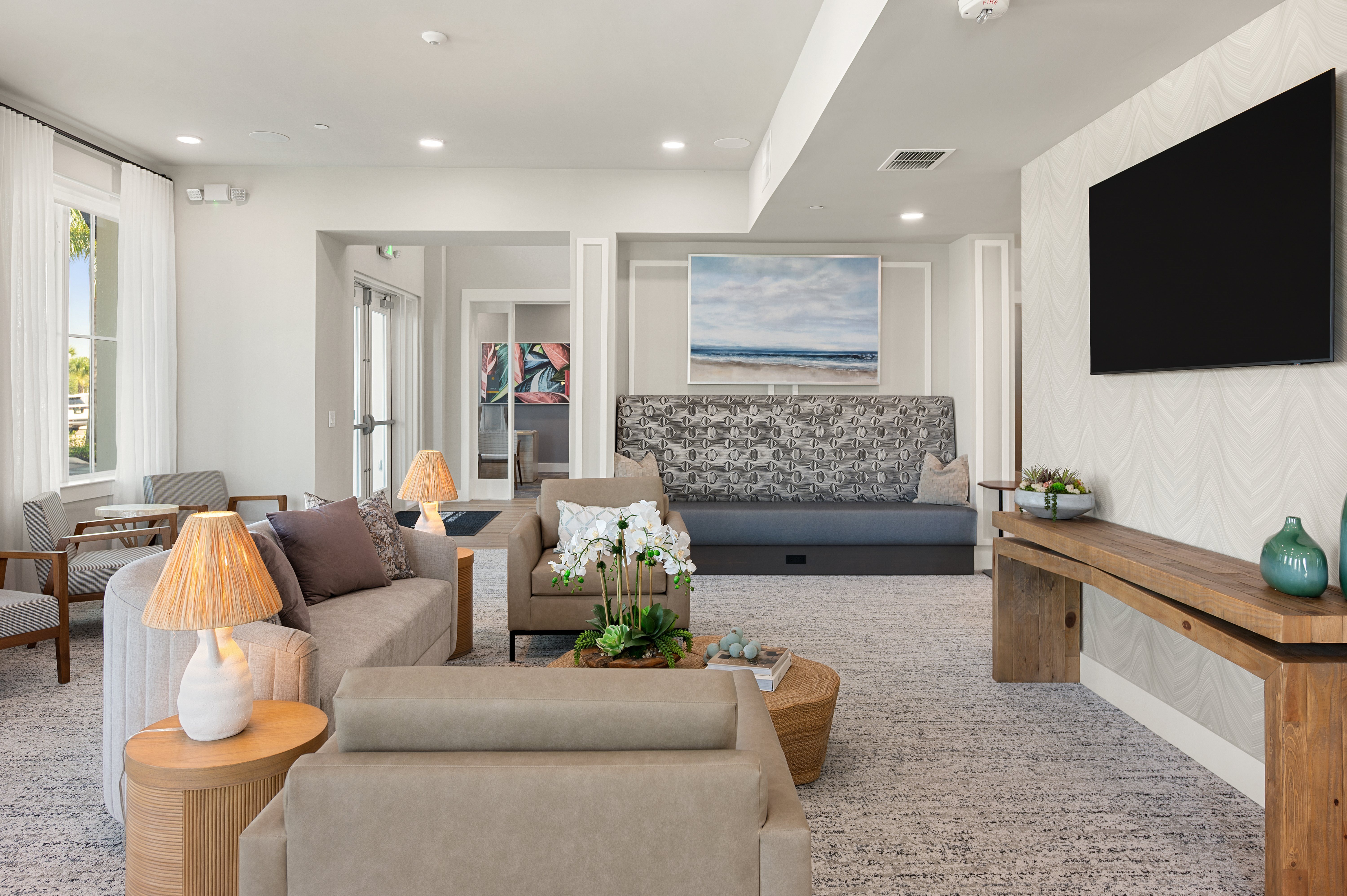 A modern living room with a grey sofa, a grey couch, a wooden coffee table, a lamp, a painting, a flat screen TV, and a vase.