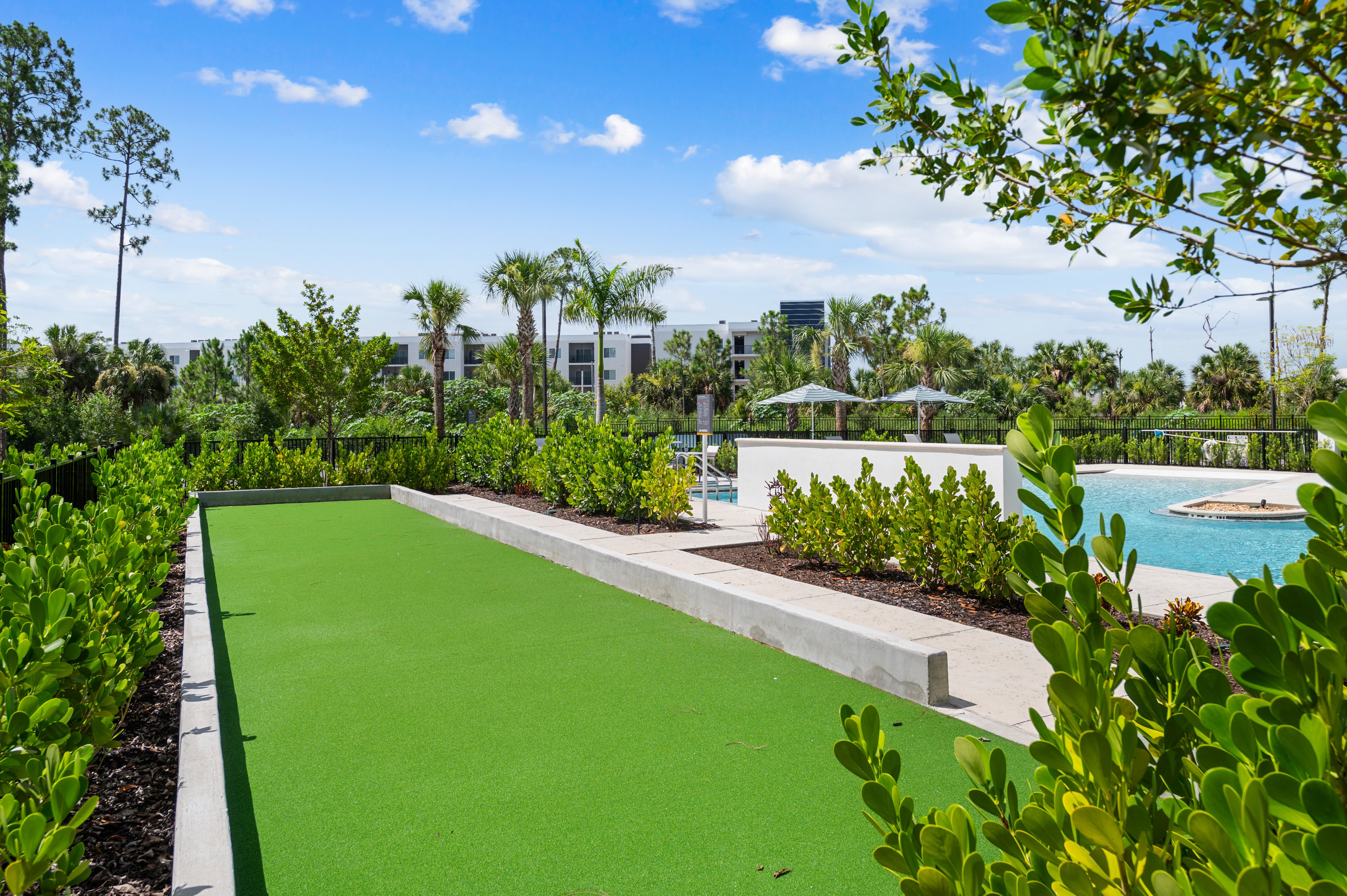 A green artificial turf is surrounded by shrubs and trees.