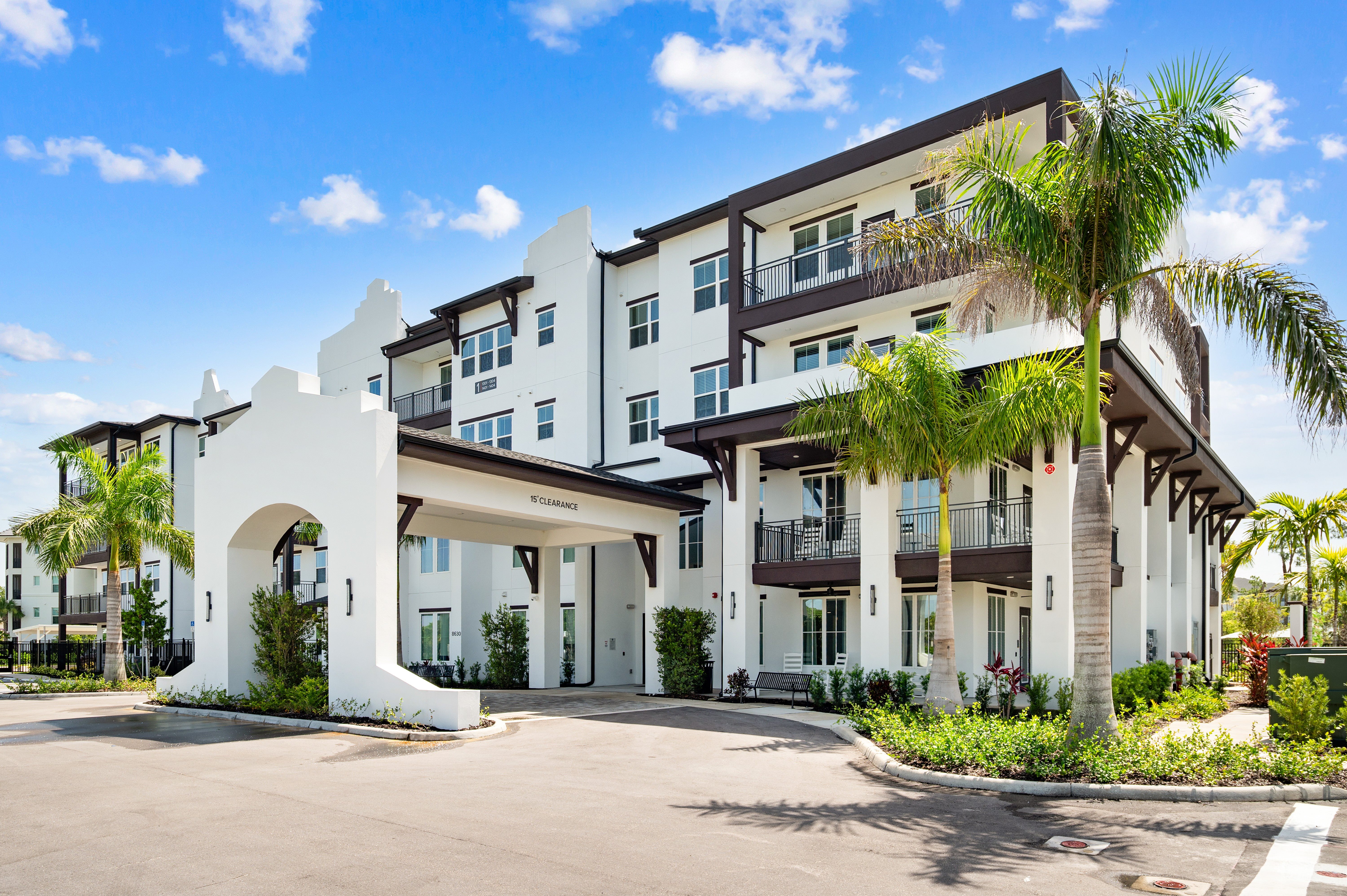 A white building with a balcony and a palm tree in front.