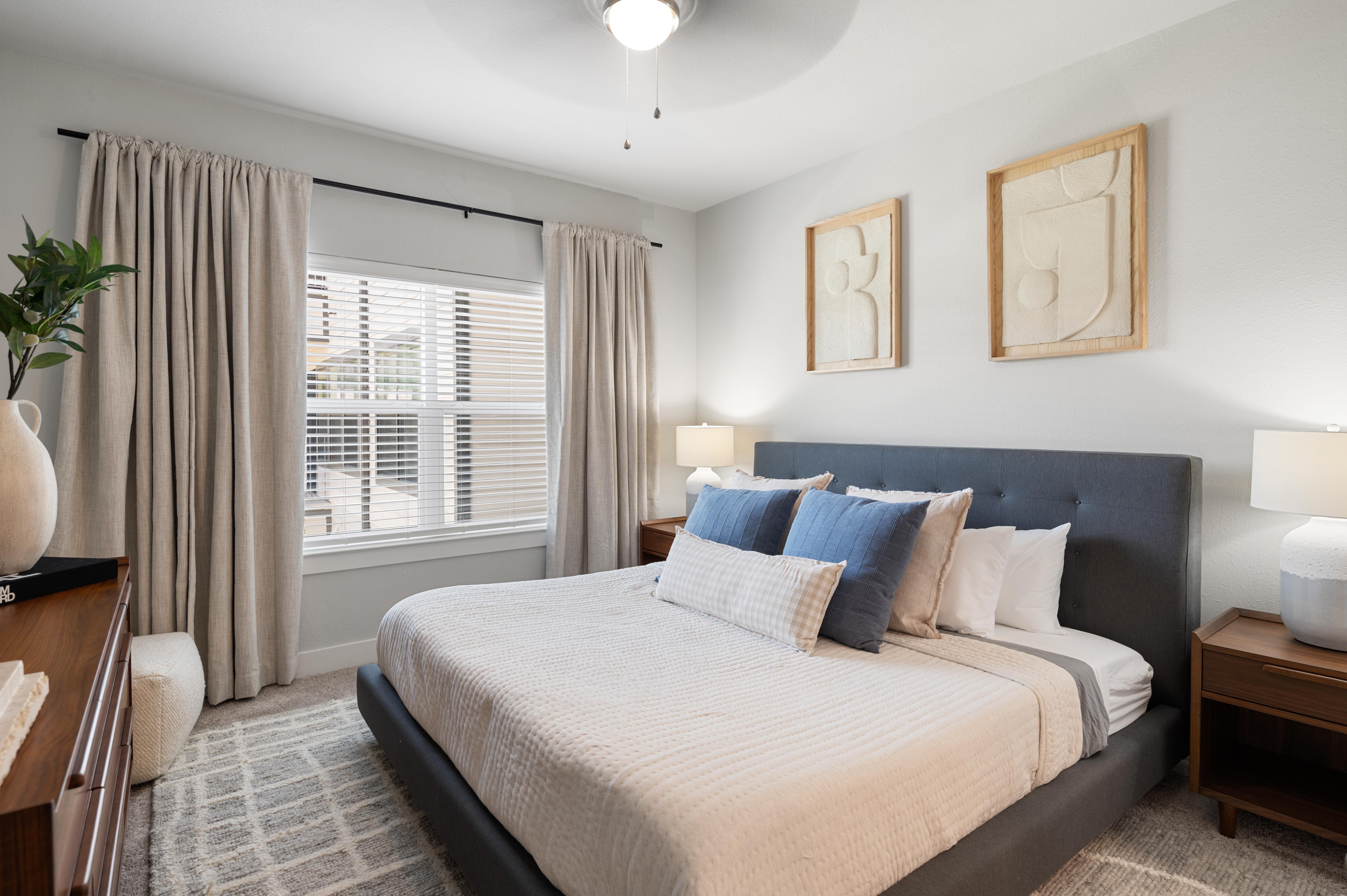 A bedroom with a large bed, a nightstand, and a window with curtains.