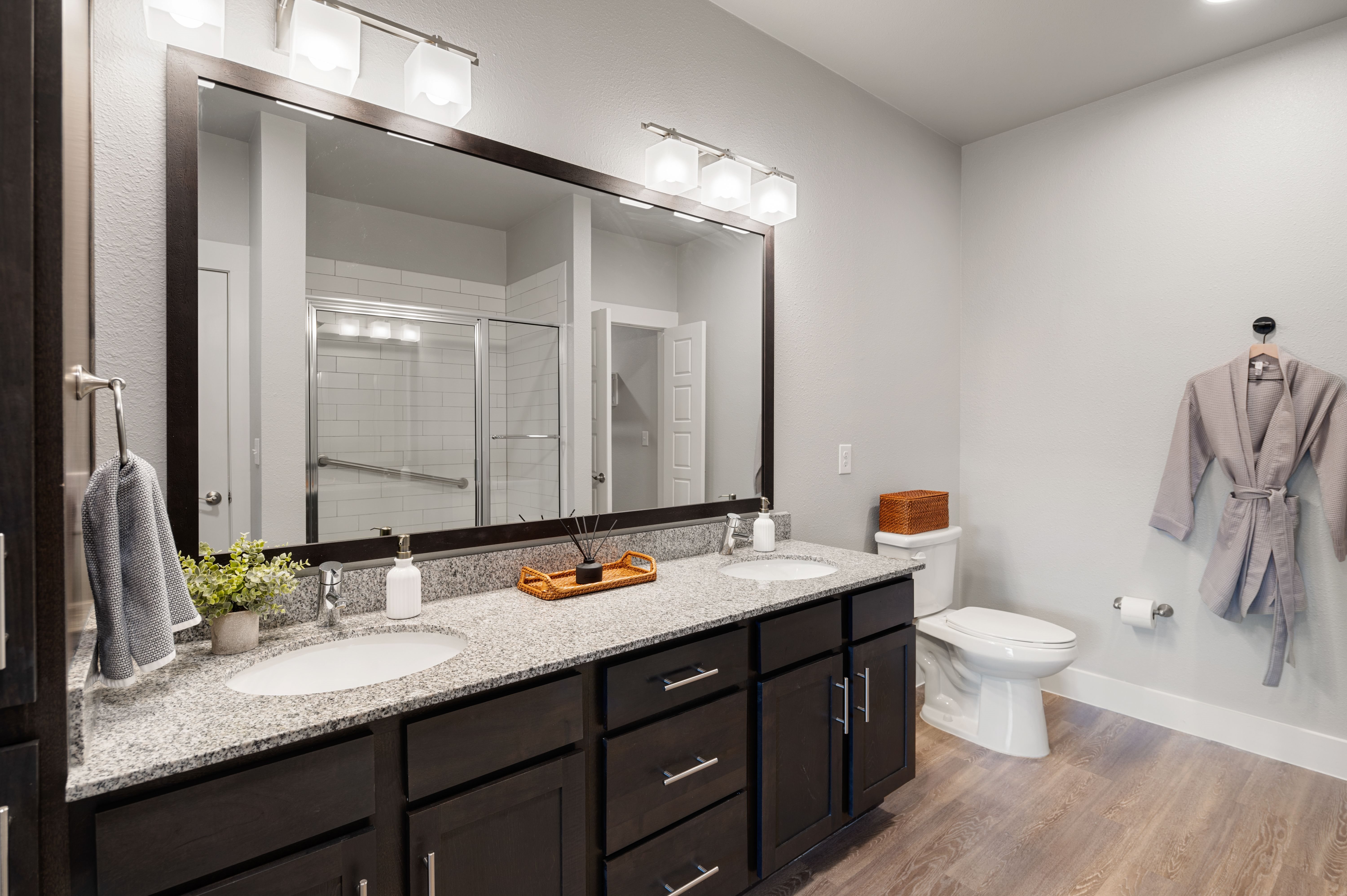 A bathroom with a sink, mirror, toilet, and a robe hanging on the wall.