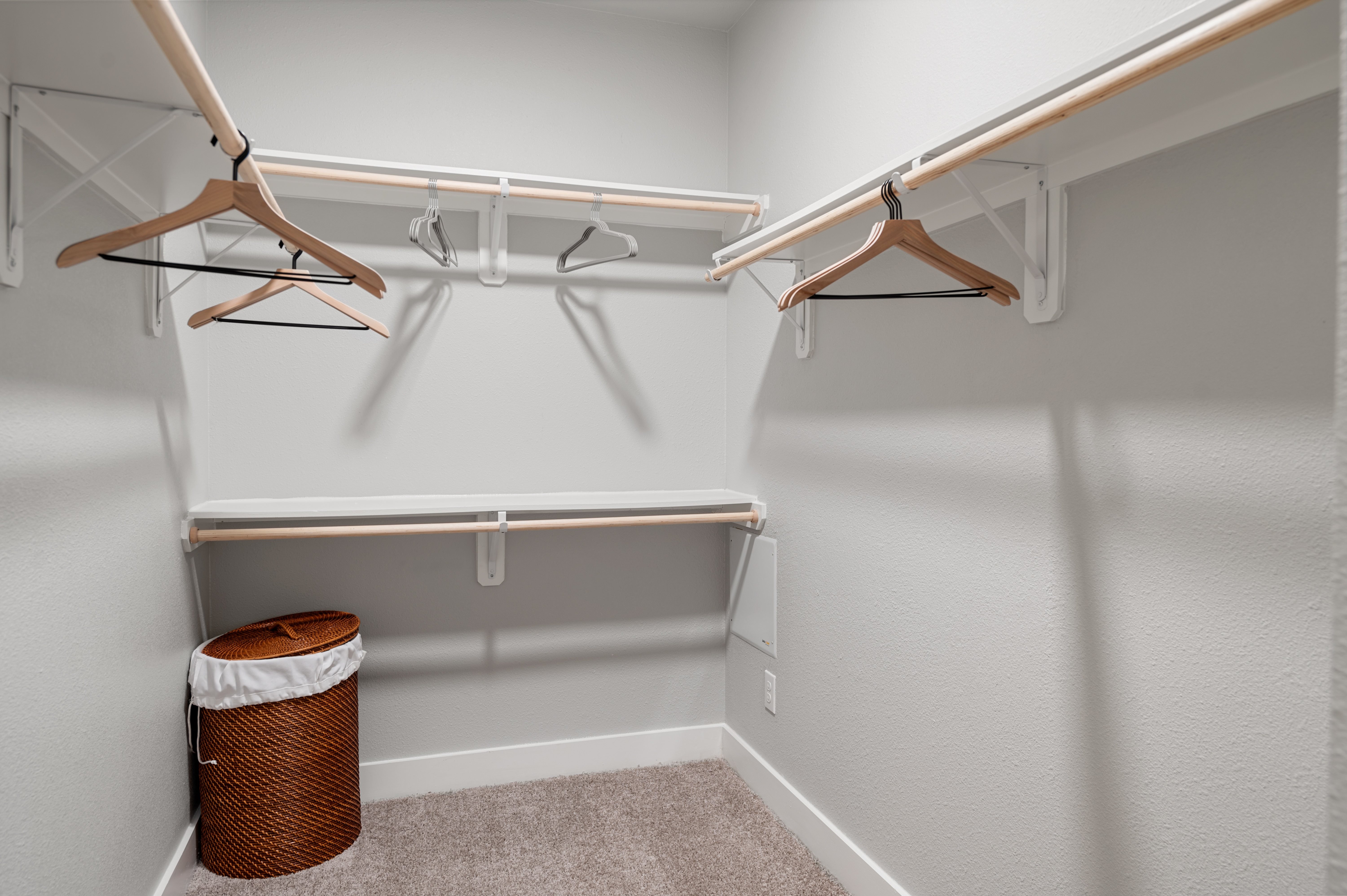 A white closet with a brown trash can and hangers.