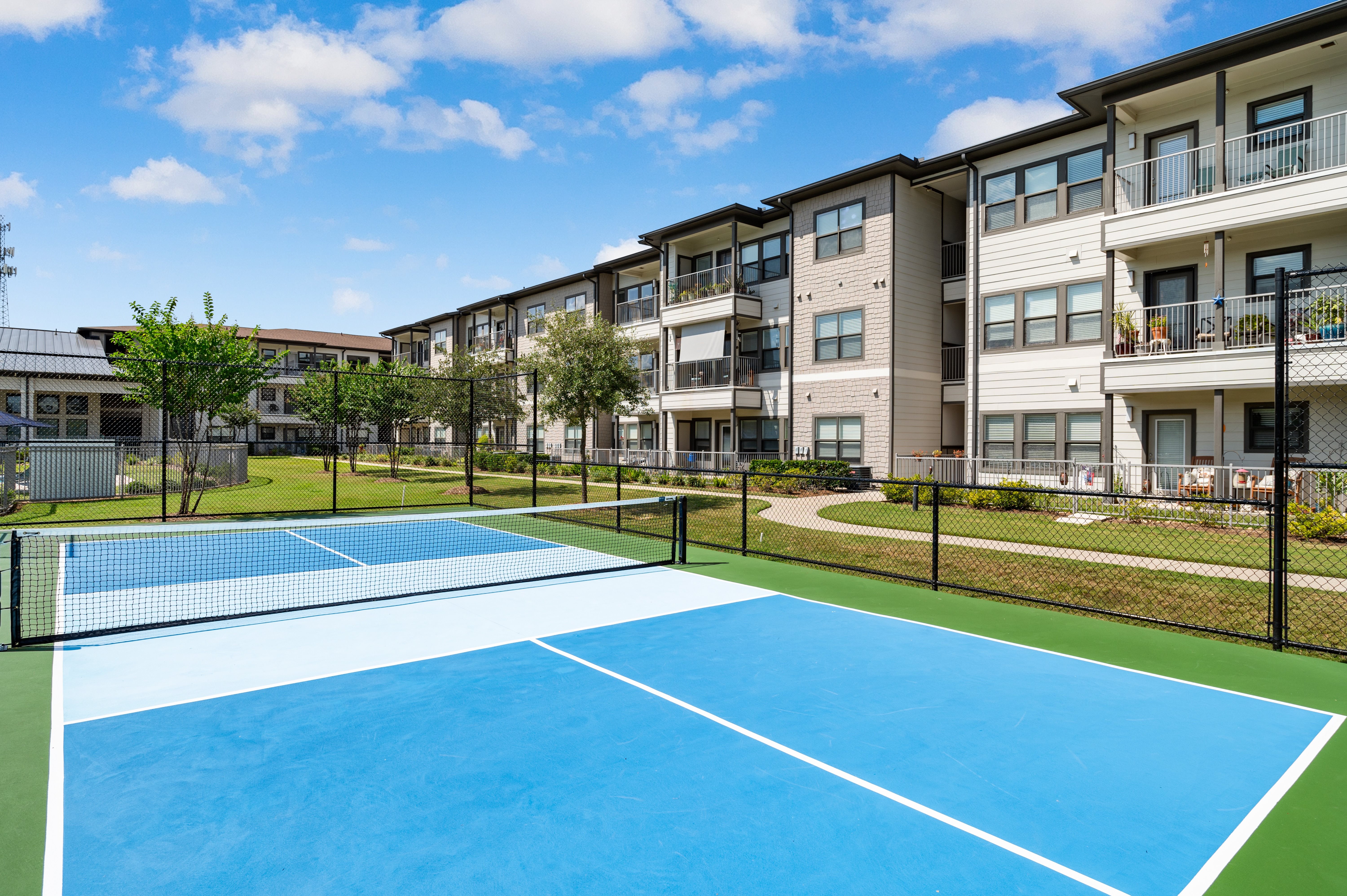 A tennis court is surrounded by apartment buildings.