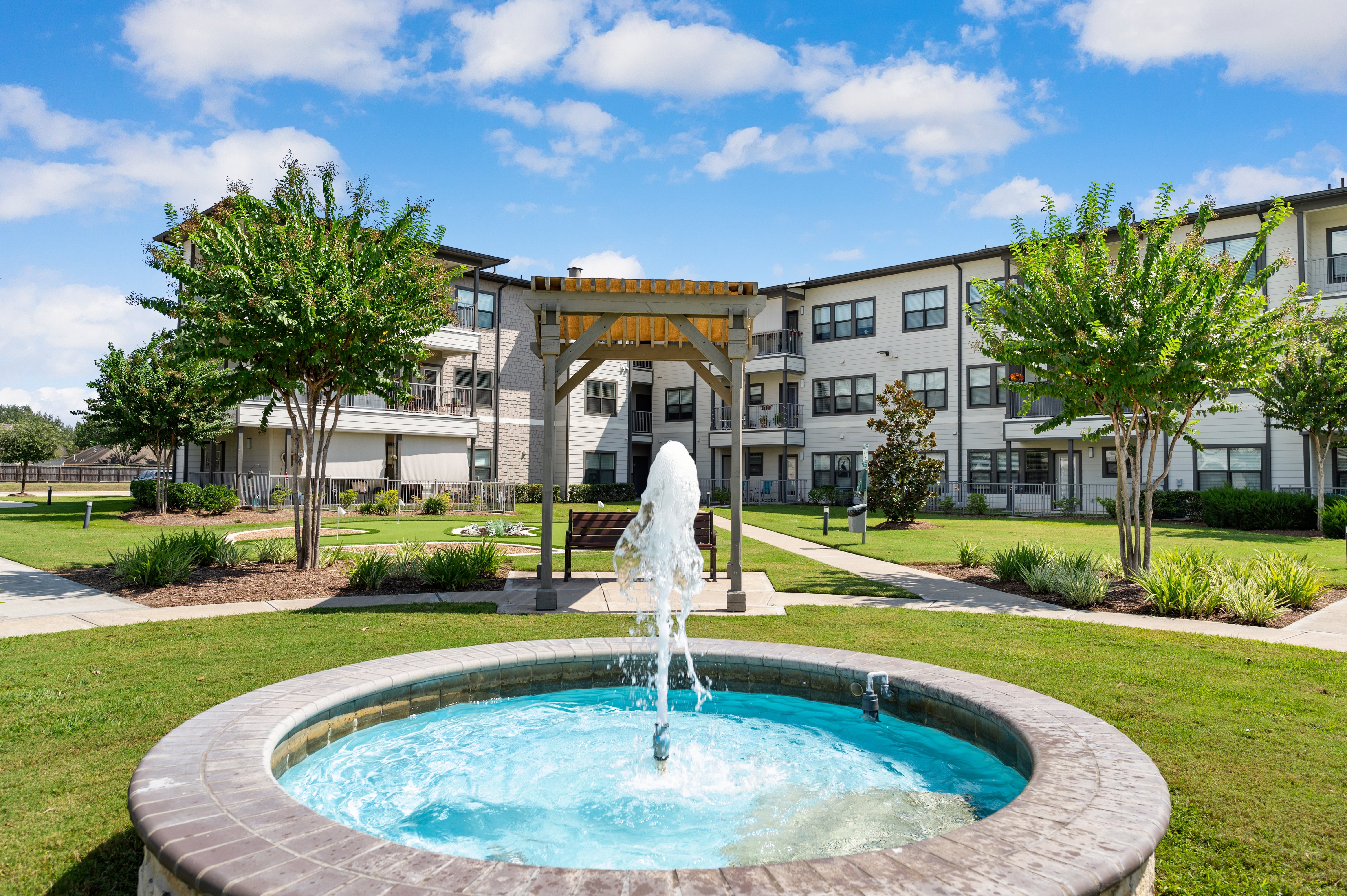 A fountain in the middle of a grassy area in front of a building.